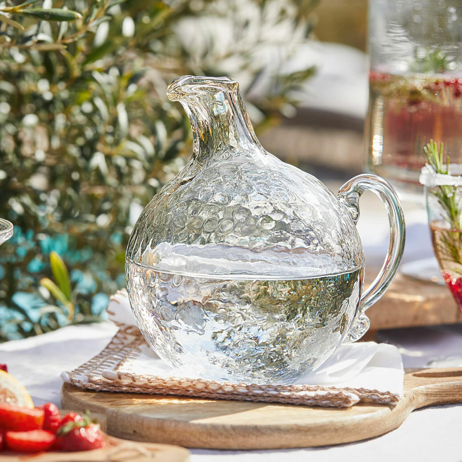 Cruche Valters Carafe en verre texturé à bulles, transparente, posée sur une planche en bois, pour boissons fraîches.