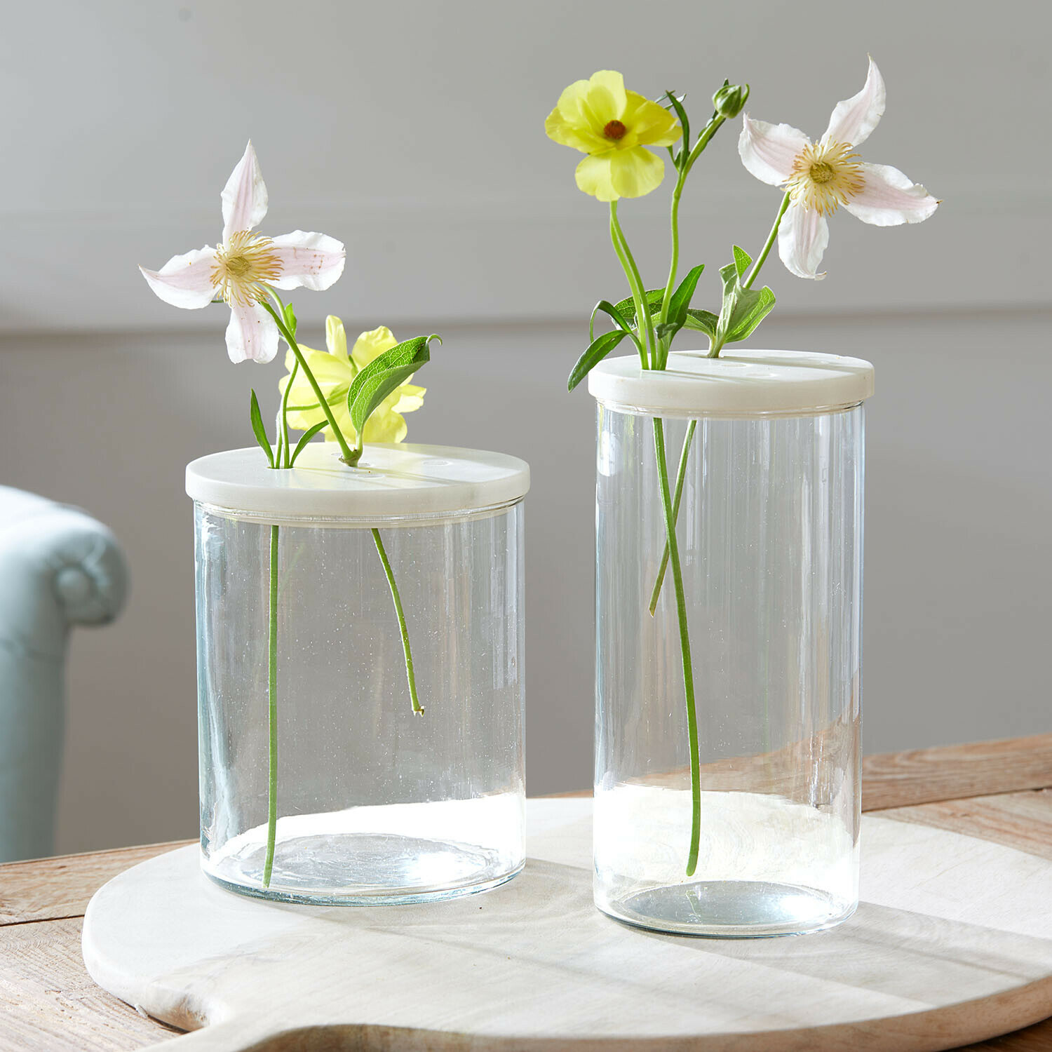 Lot de 2 pots en verre Rosanella Deux vases en verre transparents avec couvercles blancs et fleurs claires sur une table en bois