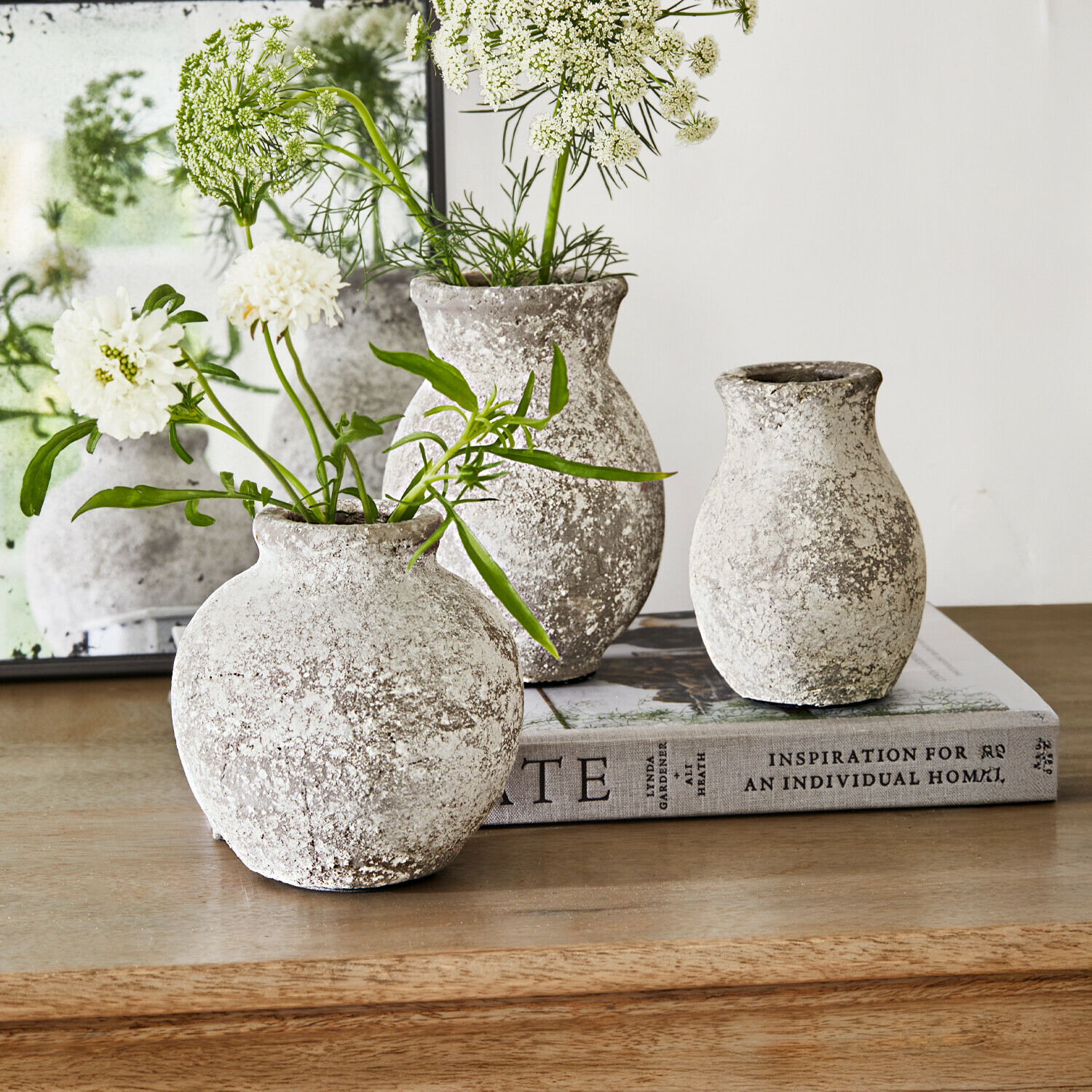 Lot de 3 vases Cerquix Trois vases rustiques en pierre gris-blanc sur une table en bois avec des fleurs blanches