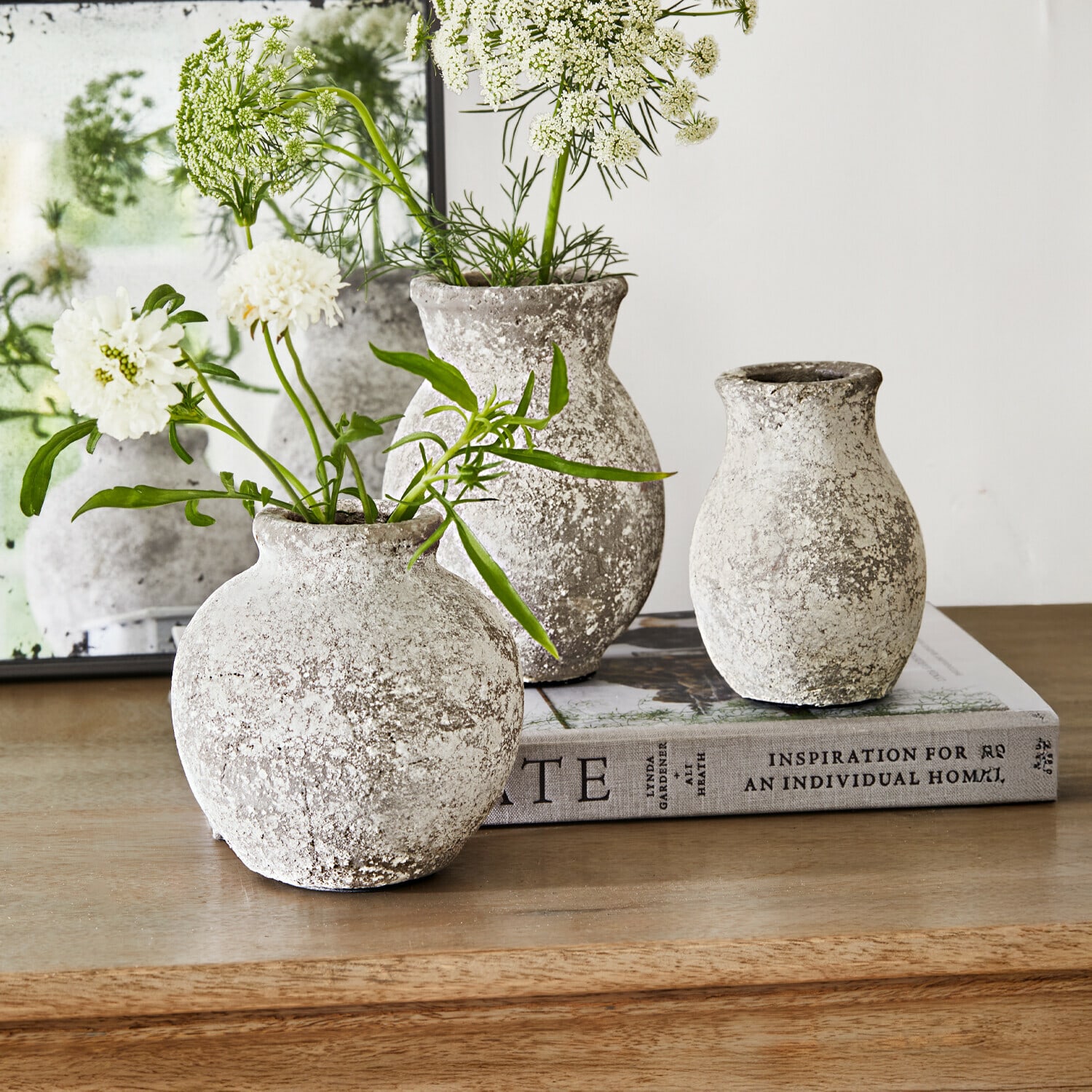 Lot de 3 vases Cerquix Trois vases rustiques en pierre gris-blanc sur une table en bois avec des fleurs blanches