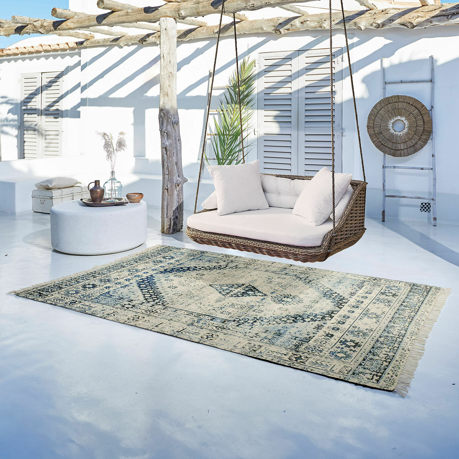 Tapis décoratif beige et bleu clair sur sol blanc avec balançoire en rotin dans un espace lumineux et moderne