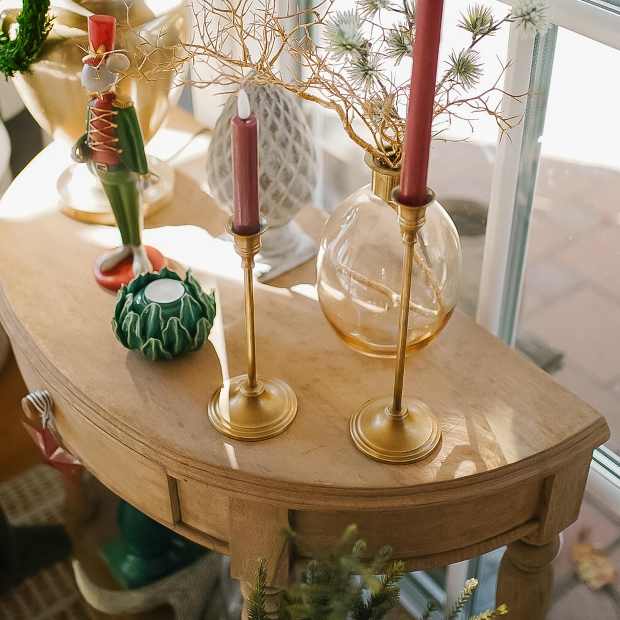 Table en bois avec deux chandeliers dorés et bougies rouges, décorations de Noël sur le dessus