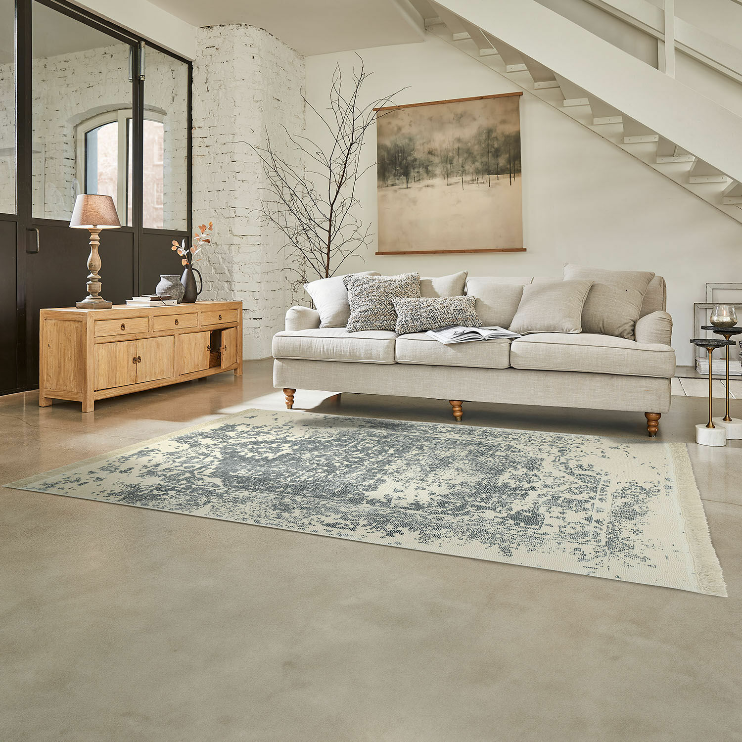 Tapis Lortet Canapé beige avec coussins sur tapis gris dans un salon lumineux avec buffet en bois et décoration murale