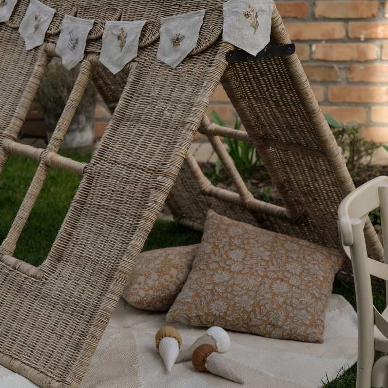 Cabane en osier avec coussins et guirlande en lin brodée dans un jardin, ambiance naturelle et cosy