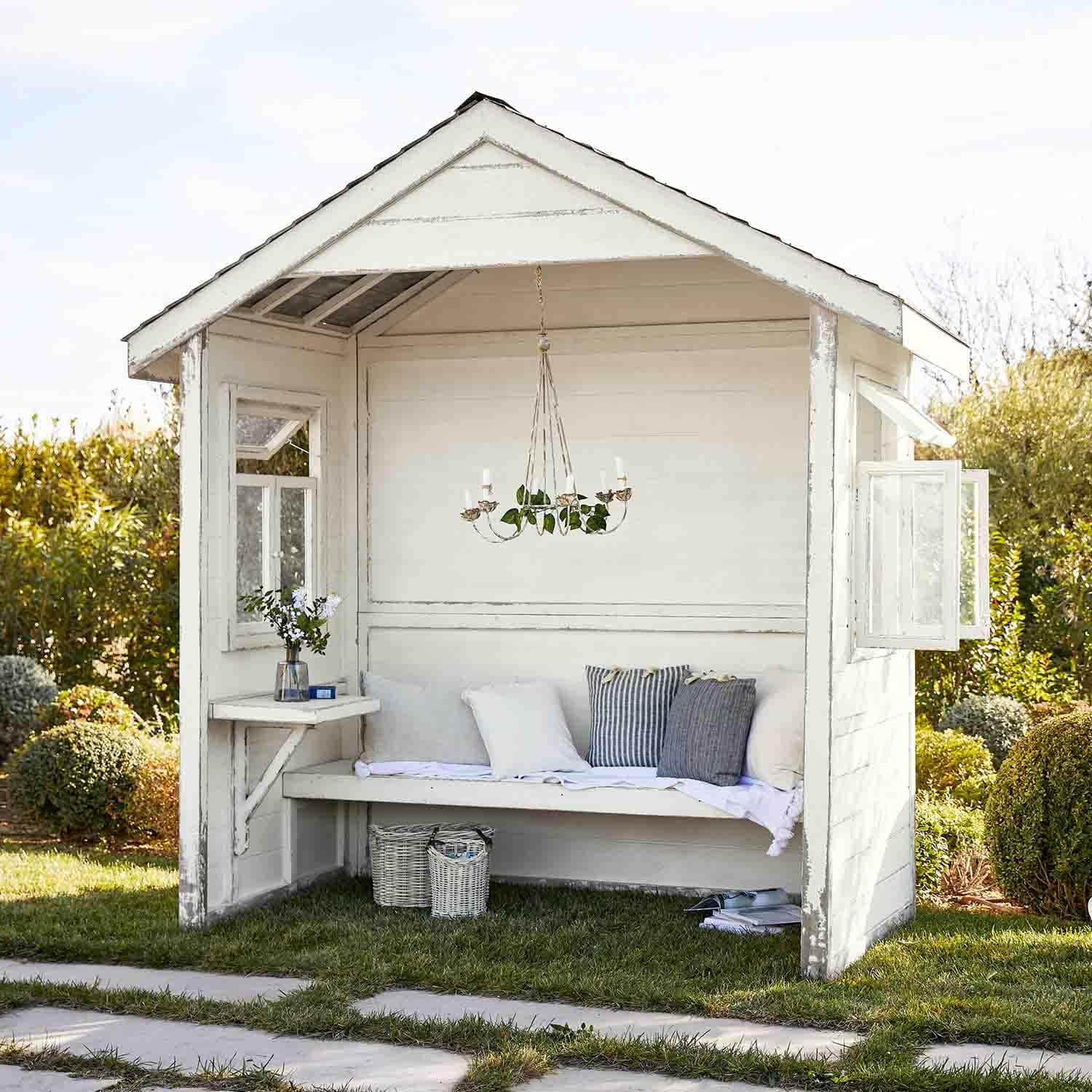 Abri de jardin en bois blanc avec banc, coussins et chandelier suspendu, espace détente extérieur