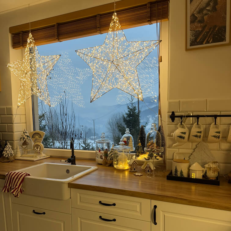 Étoiles lumineuses décoratives dans une cuisine avec plan de travail en bois et décorations de Noël devant une vue hivernale