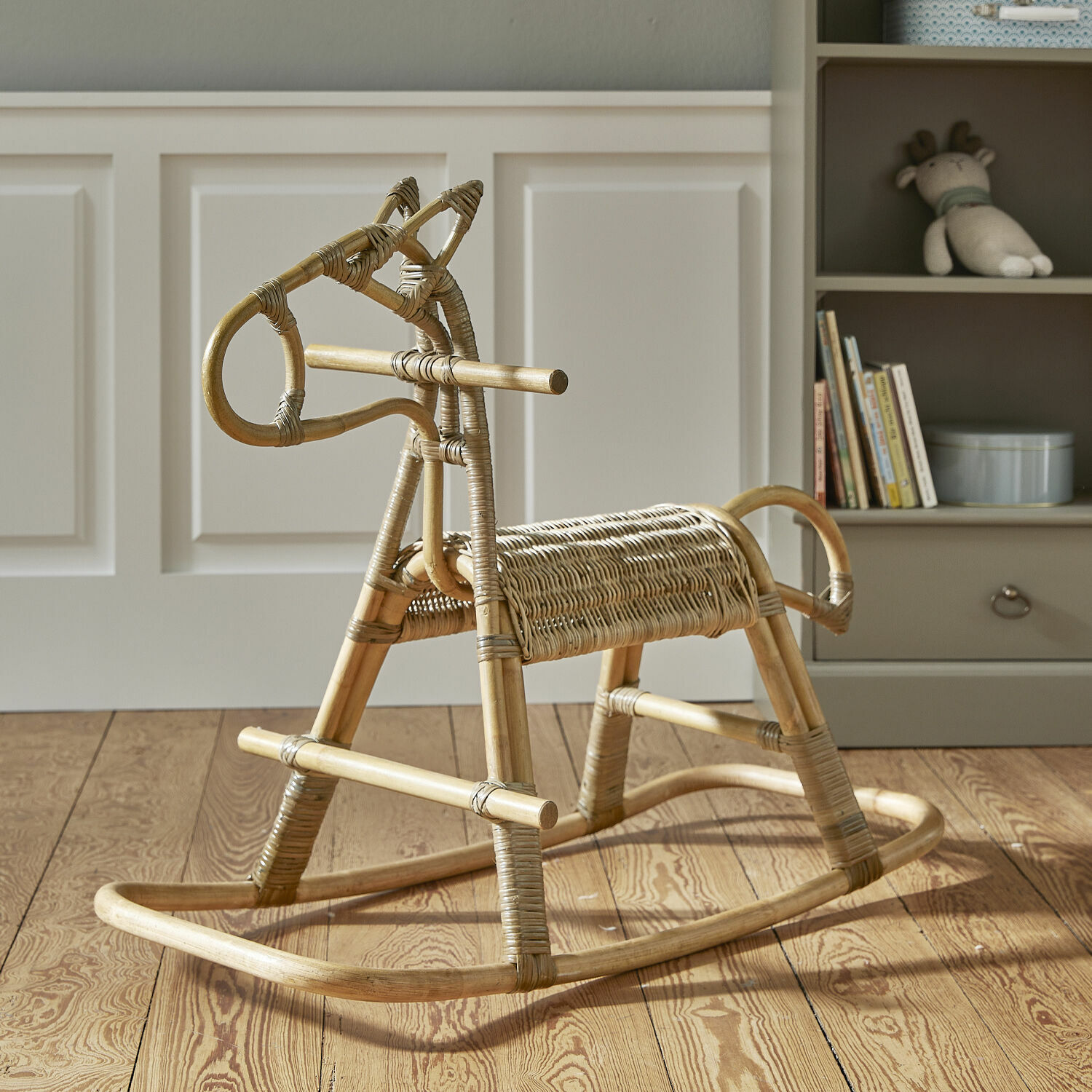 Cheval à bascule Wendeline Cheval à bascule en rotin naturel sur un sol en bois dans une chambre d'enfant