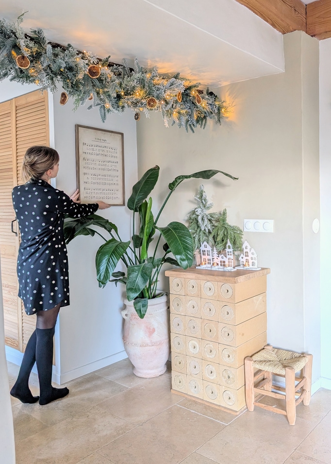 Guirlande de Noël avec tranches d'orange séchées et lumières LED au-dessus d'une commode décorée dans un intérieur clair