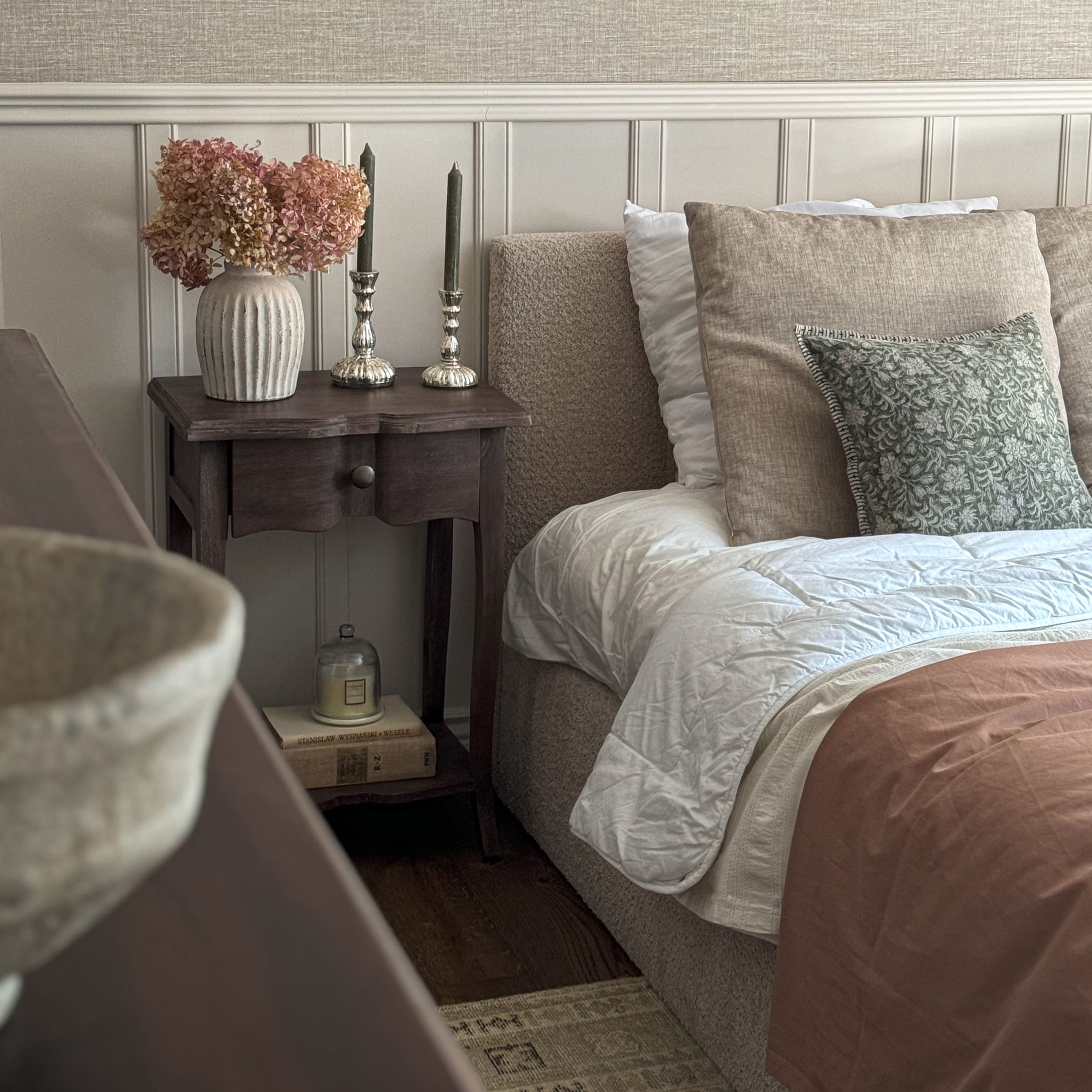 Chambre chaleureuse avec literie beige, table de chevet en bois et vase décoratif avec fleurs séchées