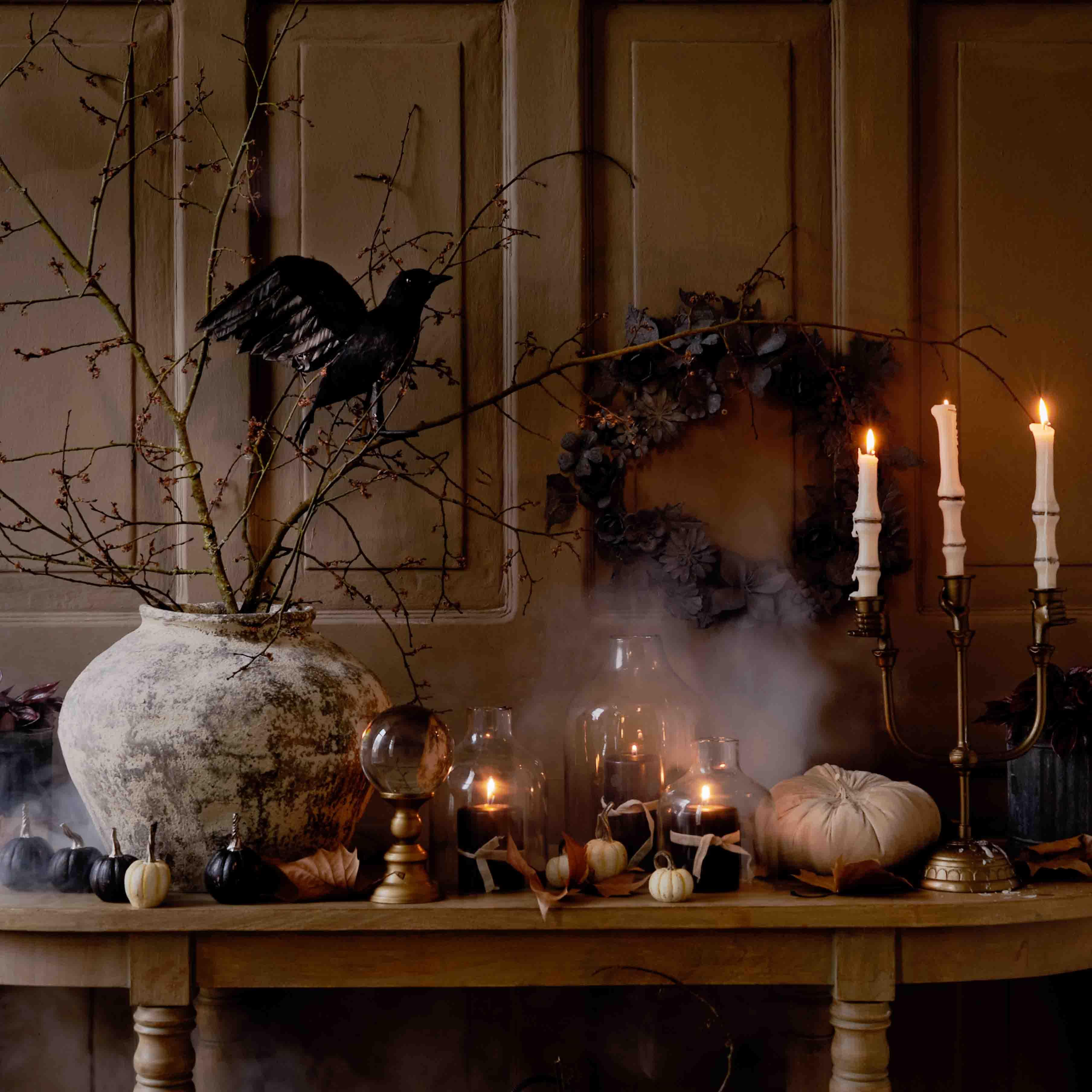 Table décorative d'automne avec grand vase en céramique, bougies allumées et oiseau noir sur branche