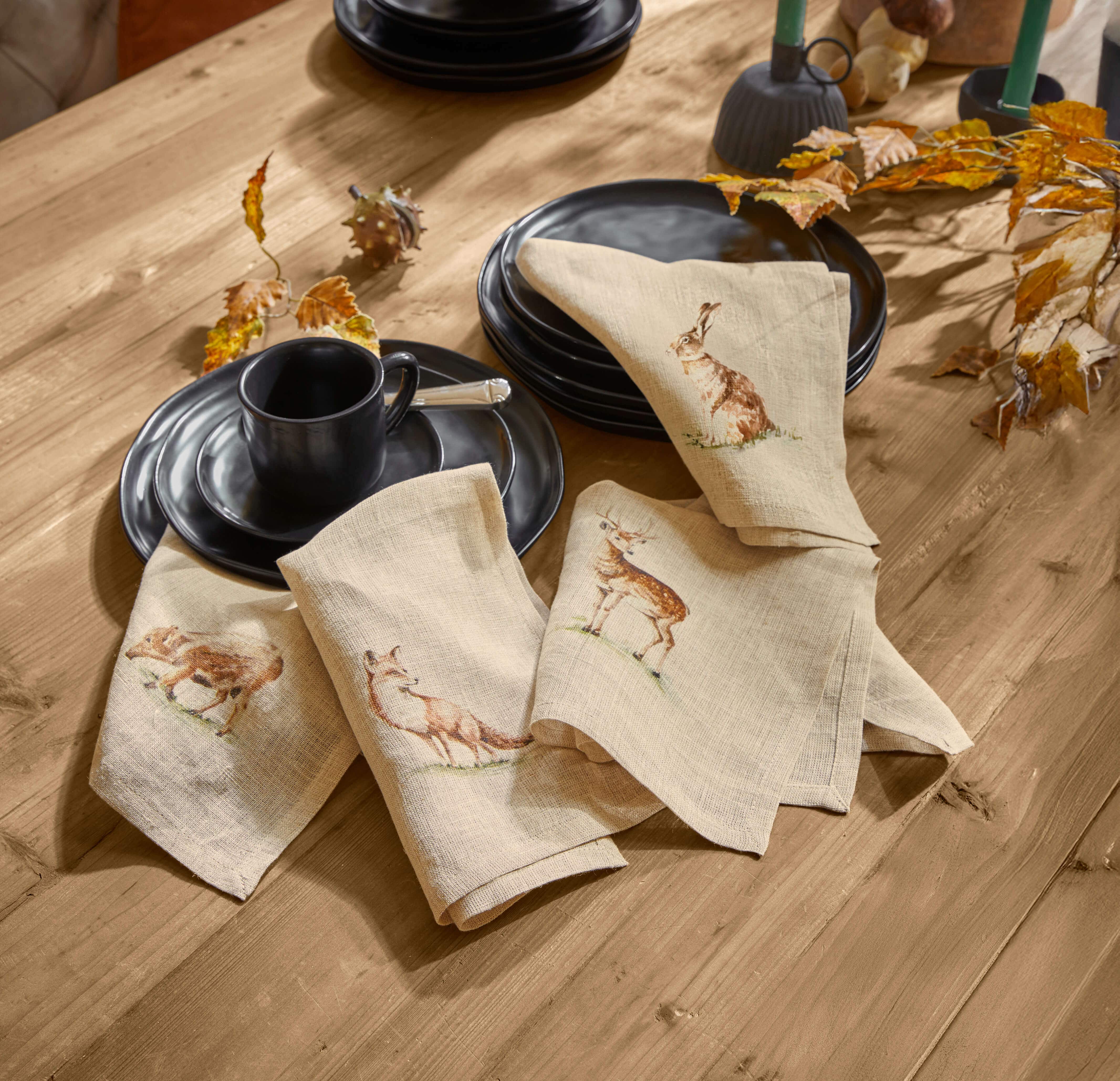 Serviettes en lin beige avec motifs d'animaux forestiers sur table en bois avec vaisselle noire