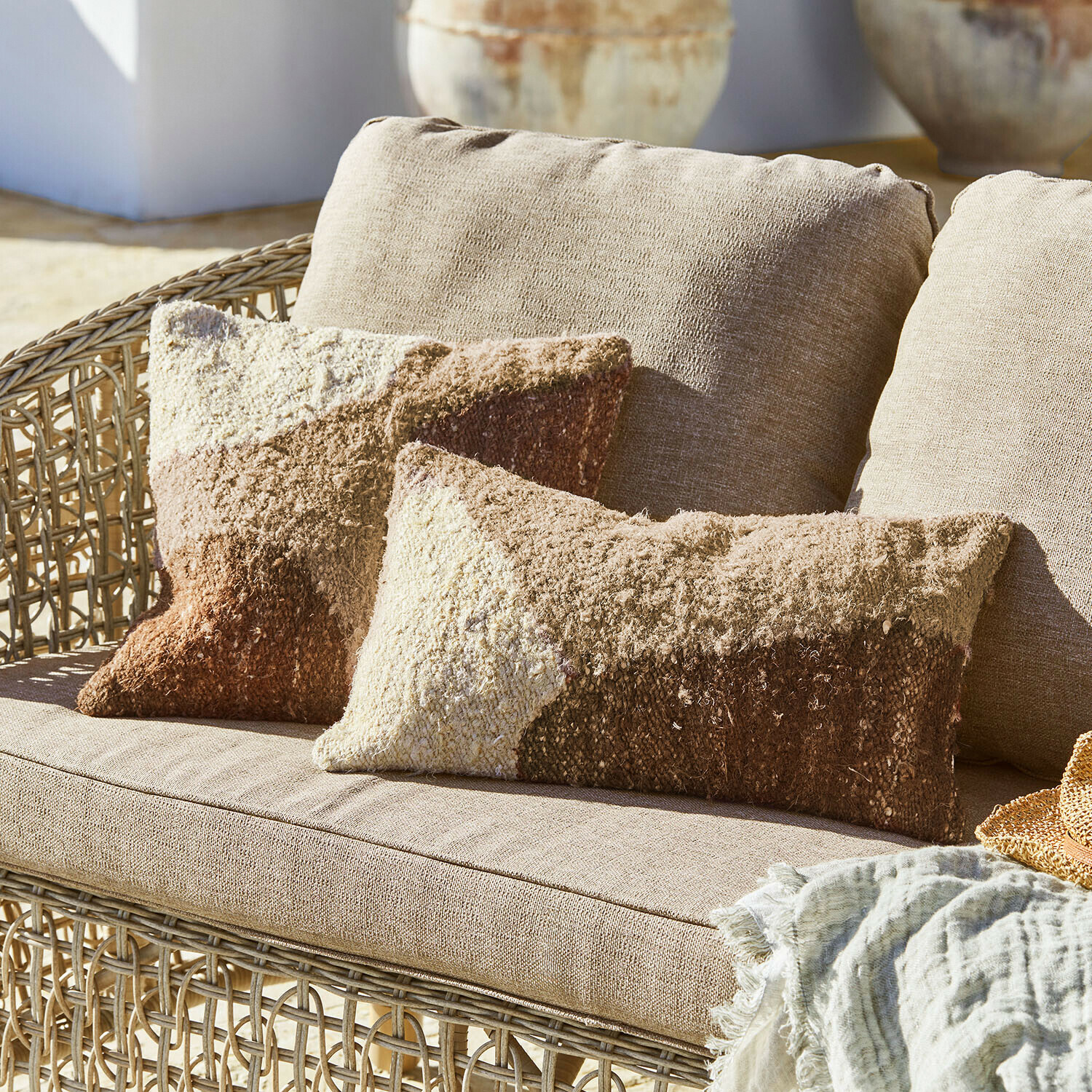 Canapé en osier beige avec coussins doux aux tons marron et crème, couverture textile décorative