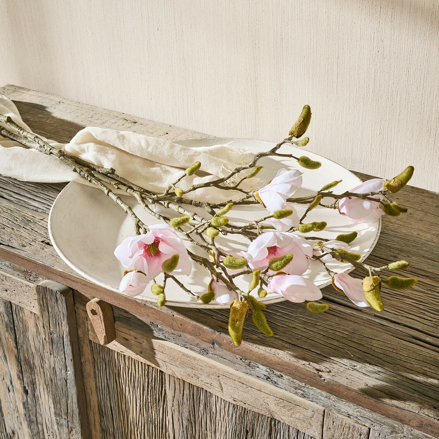 Lot de 2 fleurs décoratives Aurélines Branches de magnolia avec fleurs roses et bourgeons verts sur une assiette blanche sur un meuble en bois