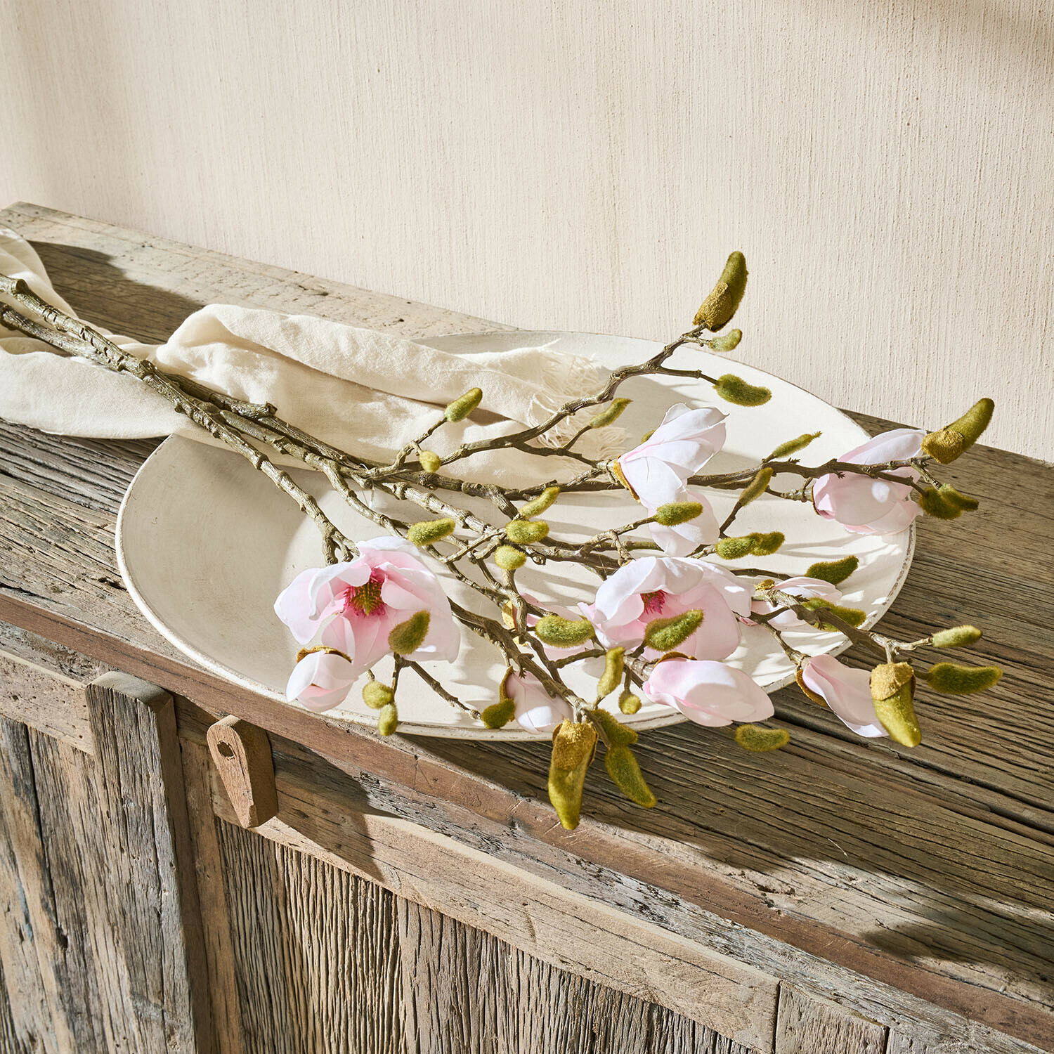 Lot de 2 fleurs décoratives Aurélines Branches de magnolia avec fleurs roses et bourgeons verts sur une assiette blanche sur un meuble en bois