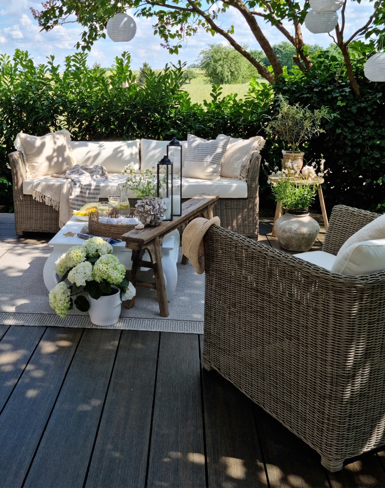 Ensemble de meubles de jardin en osier avec coussins beige sur terrasse décorée de fleurs et lanternes
