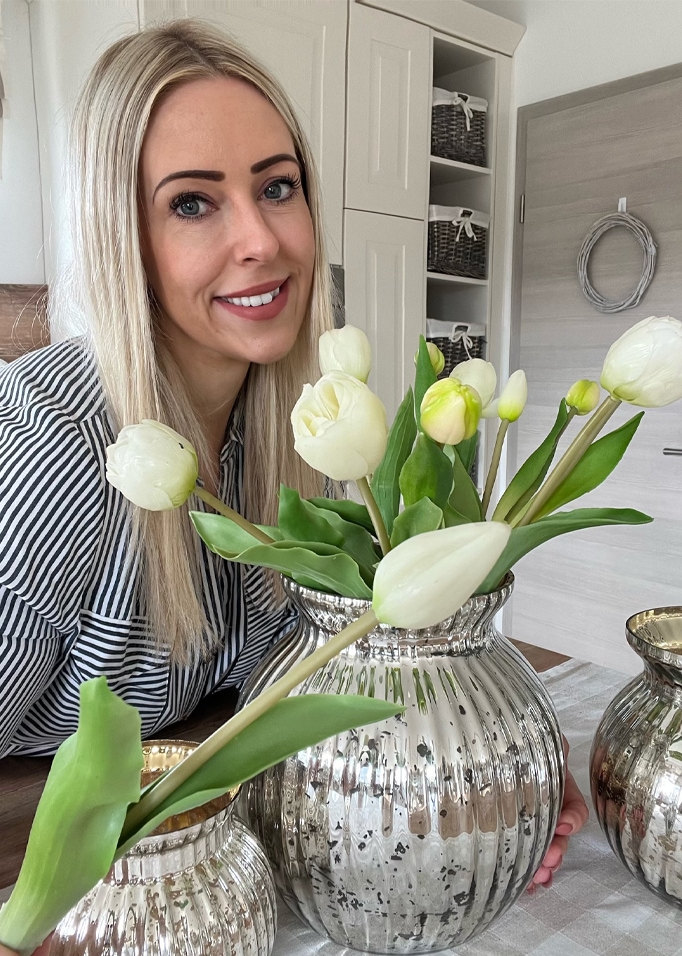 Femme aux cheveux blonds près d'un vase argenté avec des tulipes blanches dans un intérieur moderne