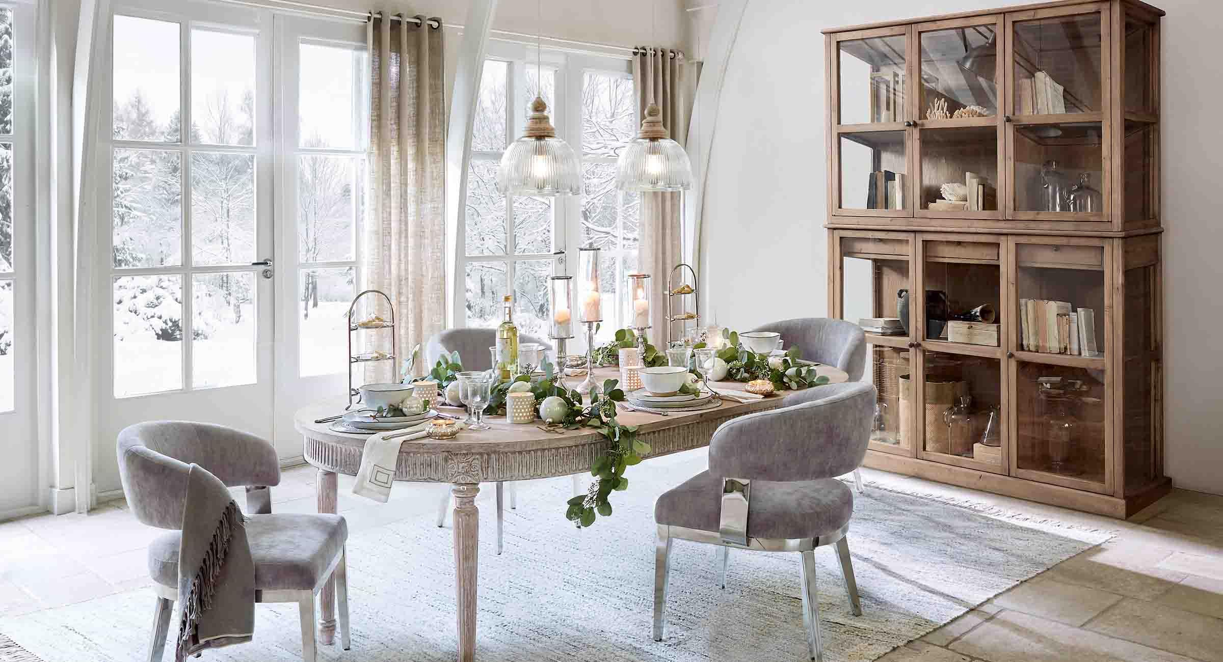 Salle à manger avec table en bois et chaises grises décorée pour l'hiver avec vue sur jardin enneigé