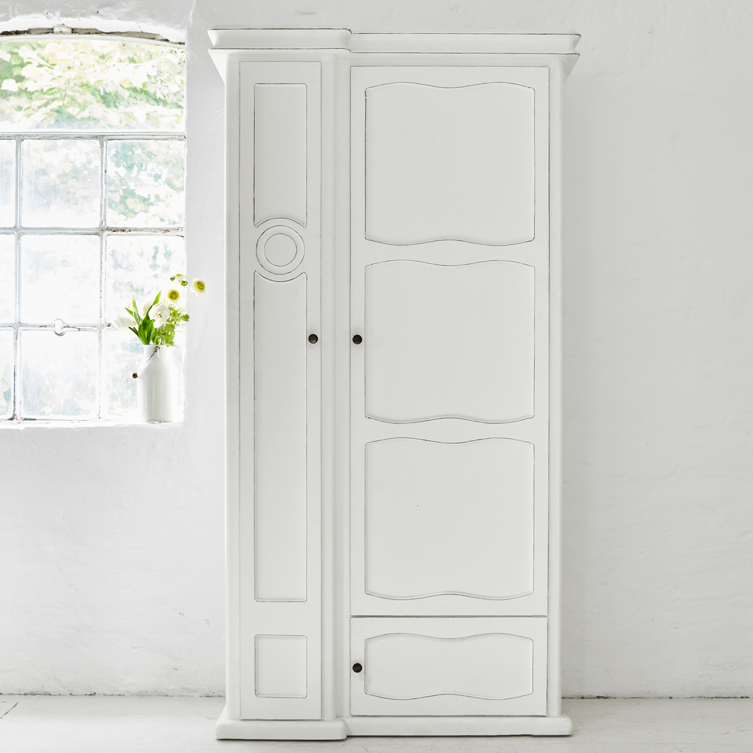 Armoire en bois blanc avec panneaux décoratifs et poignées métalliques dans une pièce lumineuse