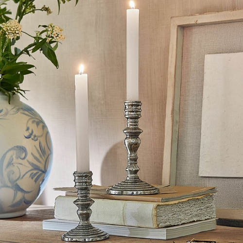 Deux bougeoirs en métal avec bougies blanches posés sur des livres anciens sur une table en bois