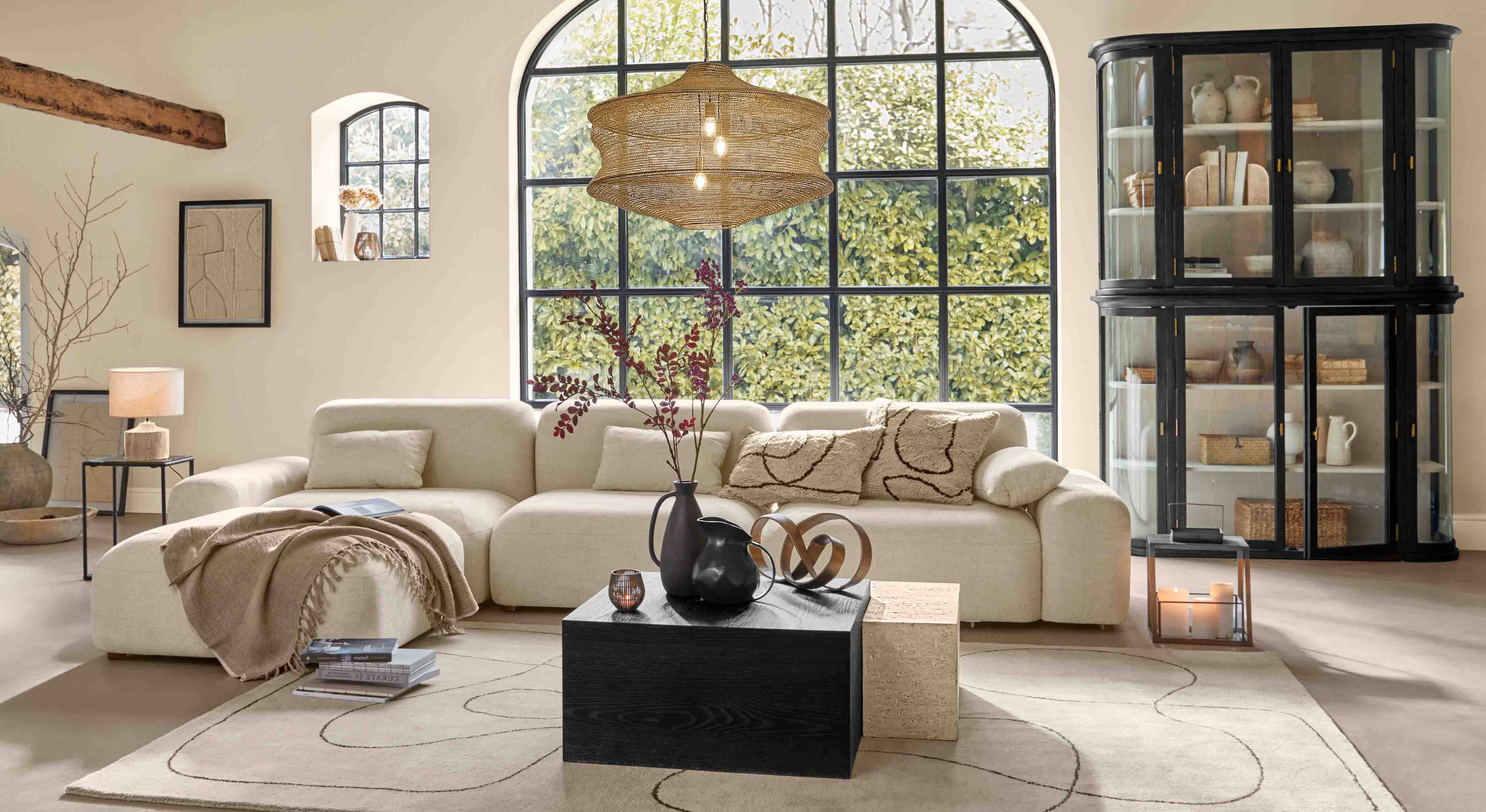 Salon chaleureux avec canapé beige, meuble noir et grande fenêtre, éclairage moderne et décorations