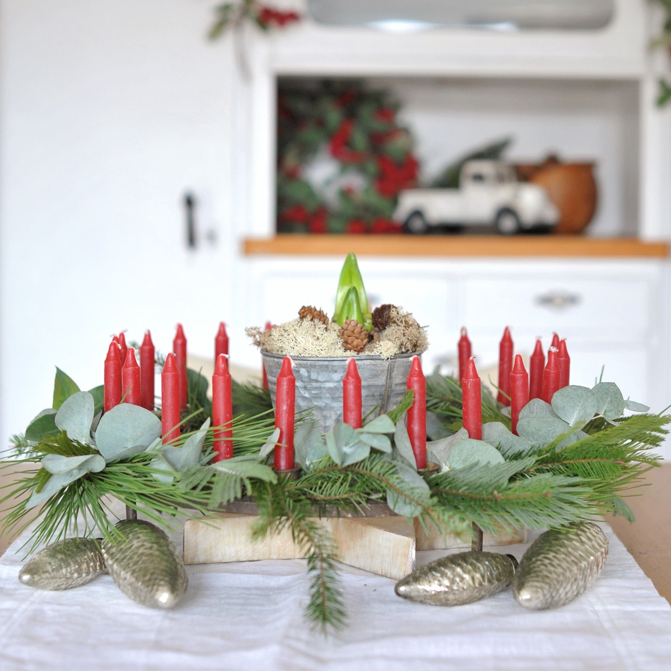 Couronne de l'Avent décorative avec bougies rouges, branches vertes et pommes de pin métalliques sur table