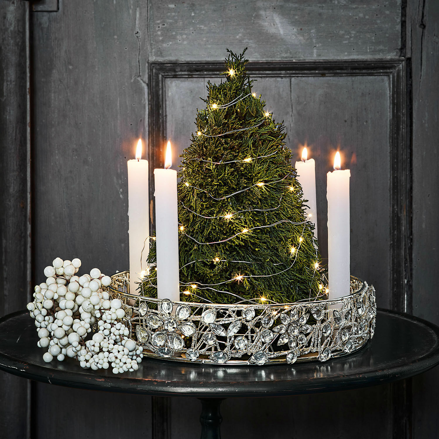 Bougeoir Hope Décoration de Noël avec sapin vert, bougies blanches et couronne argentée ornée sur une table noire
