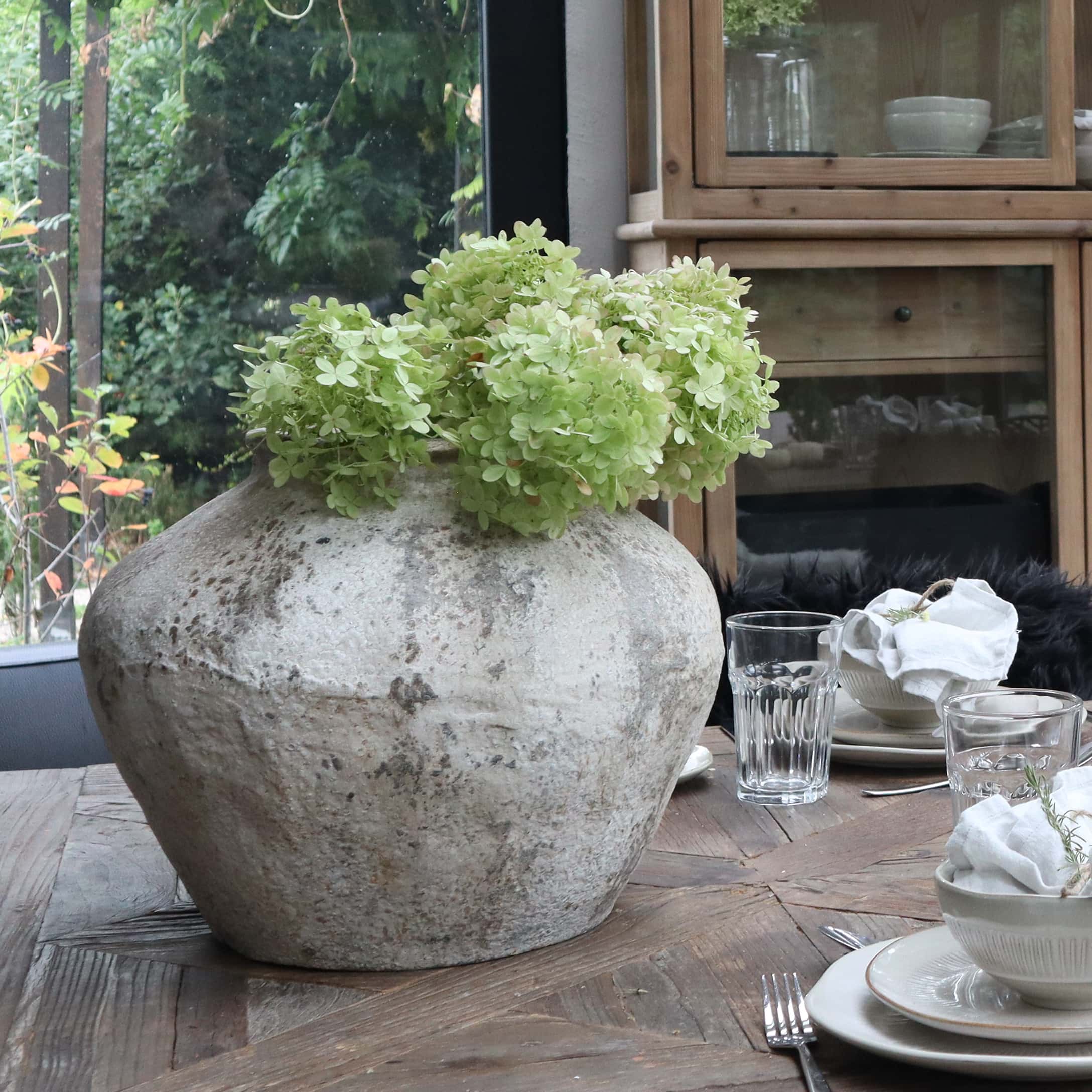 Grand vase en céramique grise avec fleurs vertes sur table en bois dans salle à manger