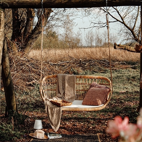 Balançoire en rotin naturel avec coussin et couverture dans un jardin d'automne