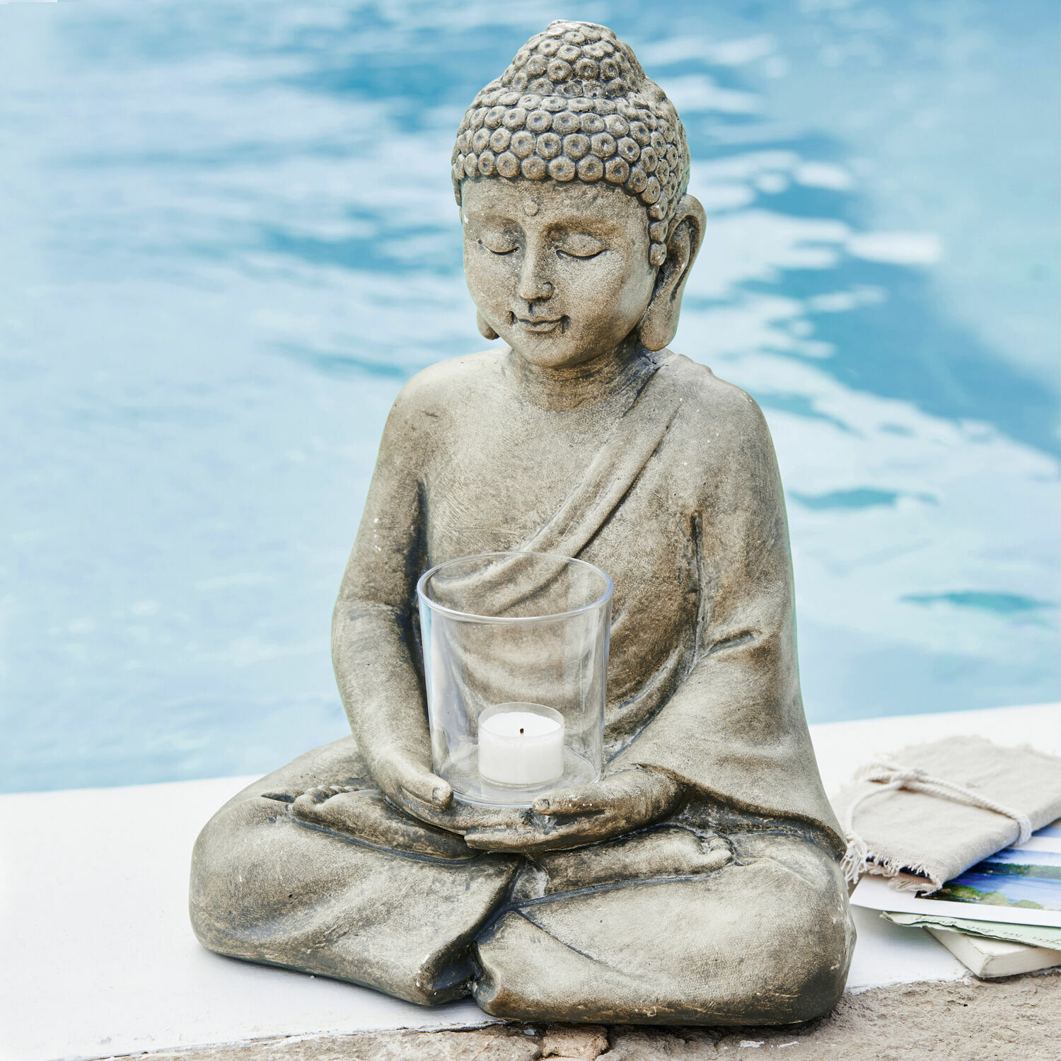 Photophore Sylvain Statue de Bouddha en pierre grise avec porte-bougie transparent pour bougie chauffe-plat au bord de la piscine