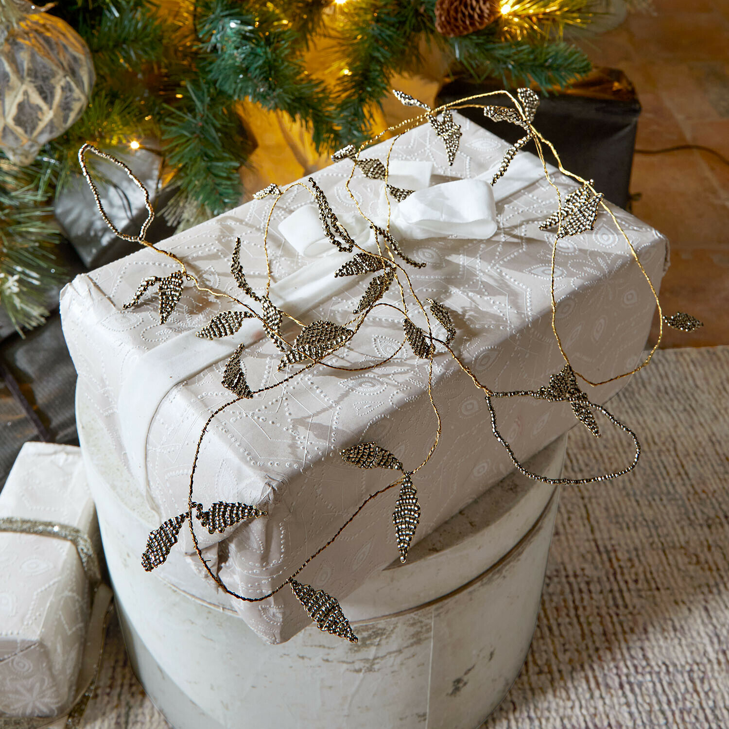 Guirlande Laymira Cadeau emballé dans un papier blanc à motif délicat avec une décoration de feuilles métalliques