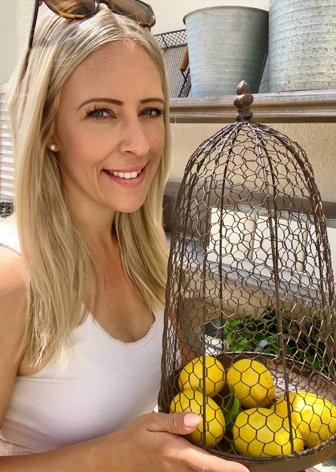 Femme tenant une cage en métal avec des citrons jaunes devant des pots en style rustique