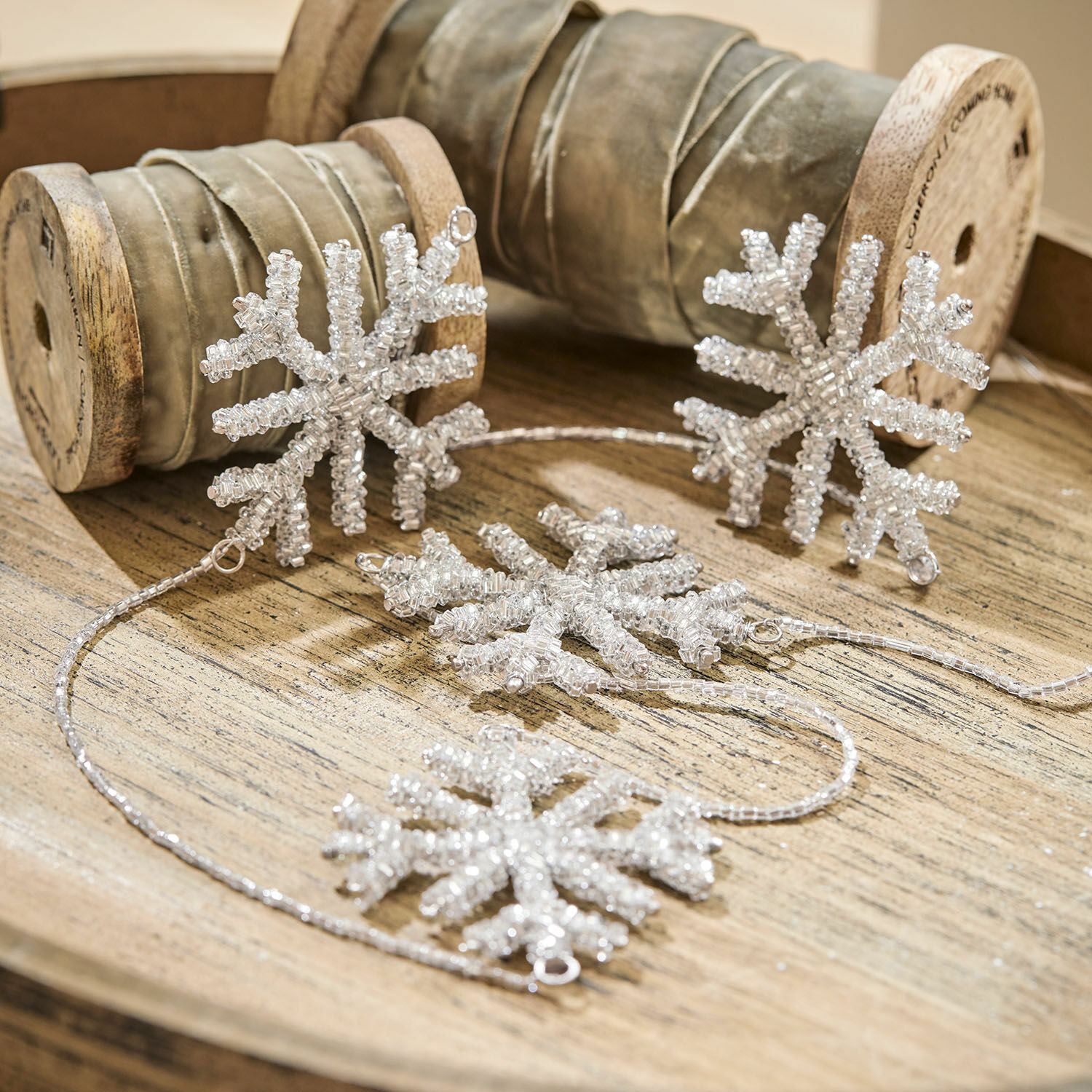 Guirlande Snowflakes Guirlande décorative de flocons de neige en perles transparentes posée sur un plateau en bois