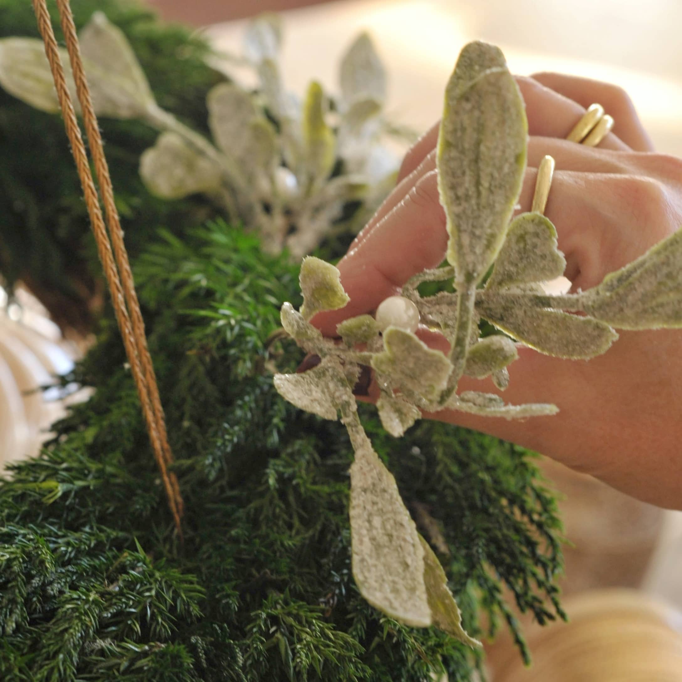 Main décorant une couronne de l'Avent blanche avec branches vertes et feuilles artificielles perlées