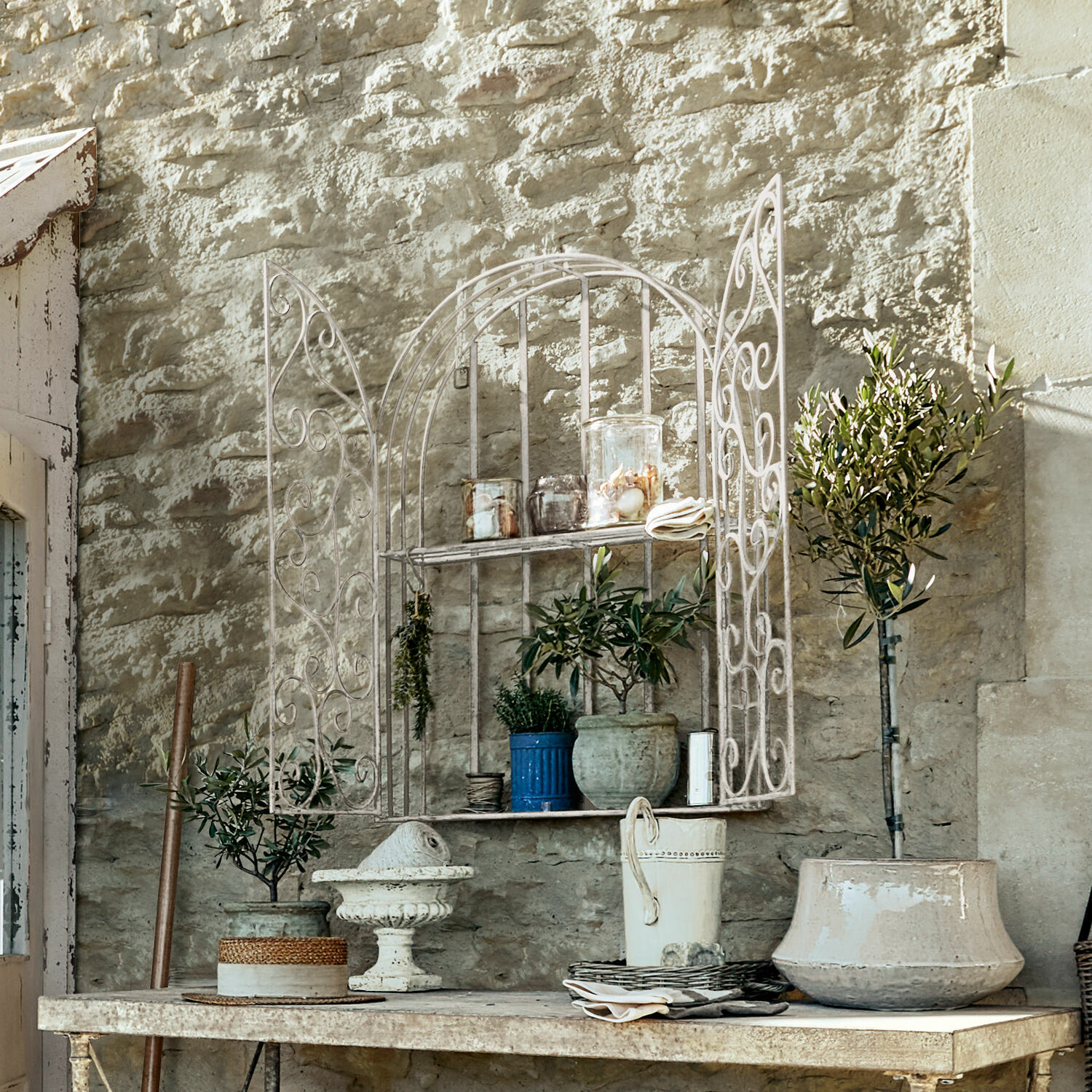 Étagère murale Chambellay Étagère murale blanche en métal avec portes décoratives et pots de fleurs devant un mur en pierre