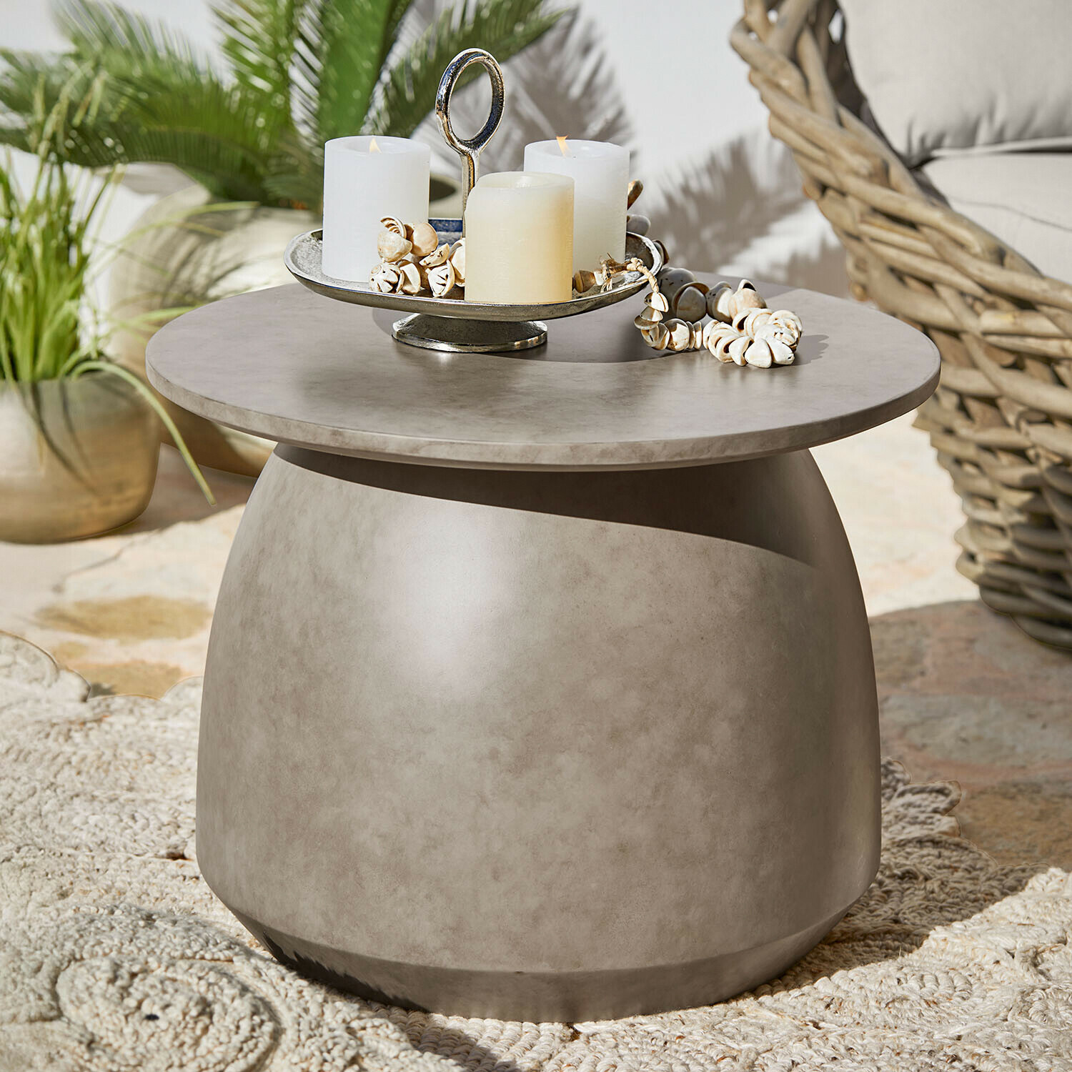 Table basse ronde en béton gris avec bougies et décorations coquillages sur terrasse extérieure