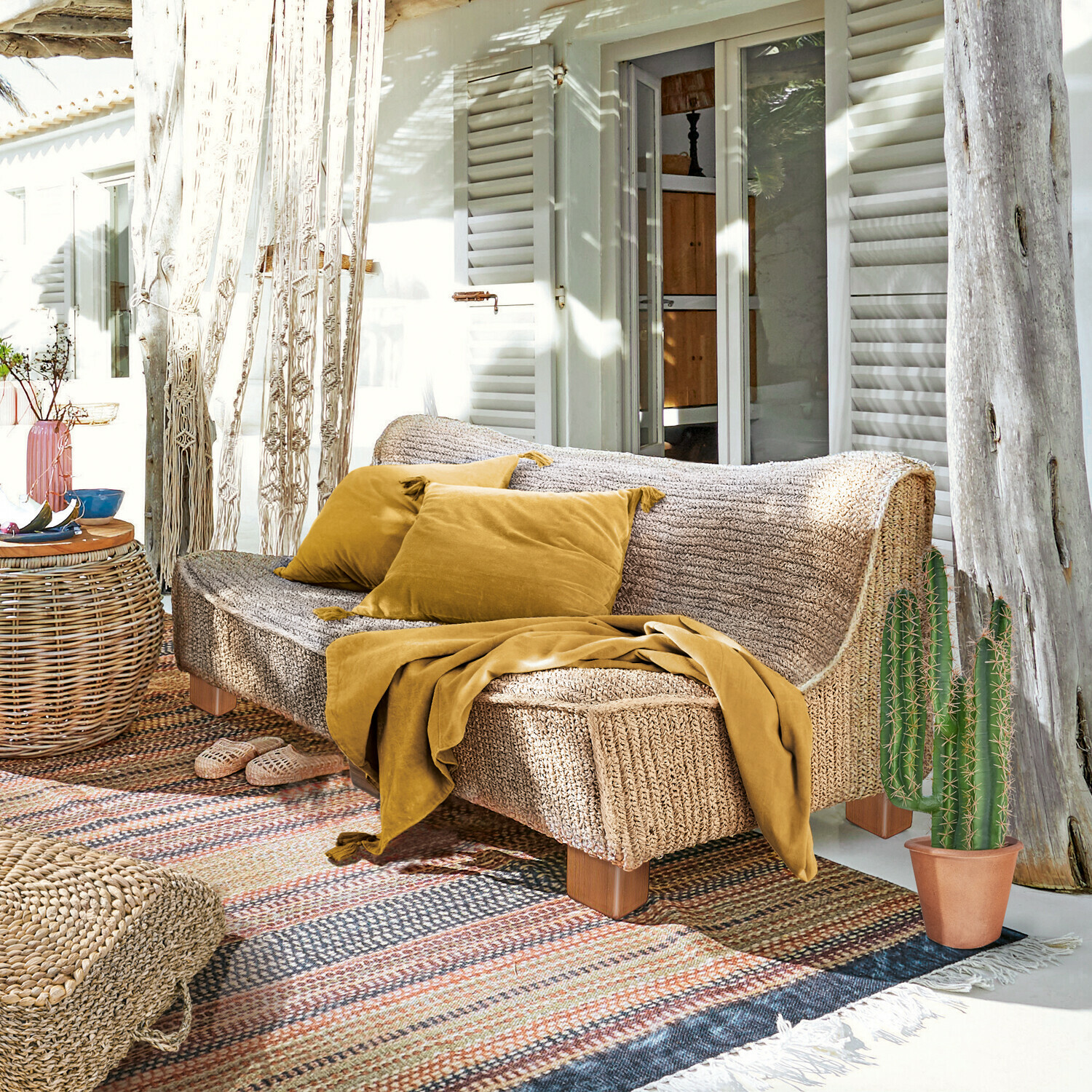 Canapé Bocage Canapé en matière tressée couleur naturelle avec coussins et plaid moutarde sur terrasse ensoleillée