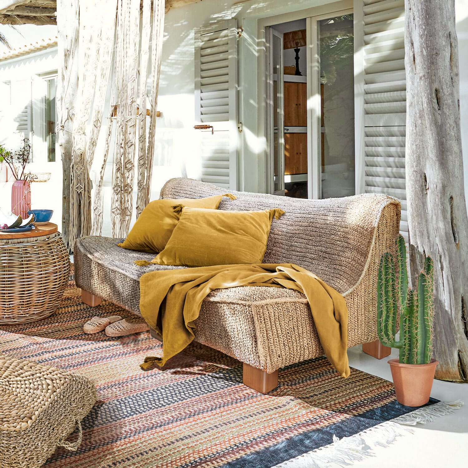 Canapé Bocage Canapé en matière tressée couleur naturelle avec coussins et plaid moutarde sur terrasse ensoleillée