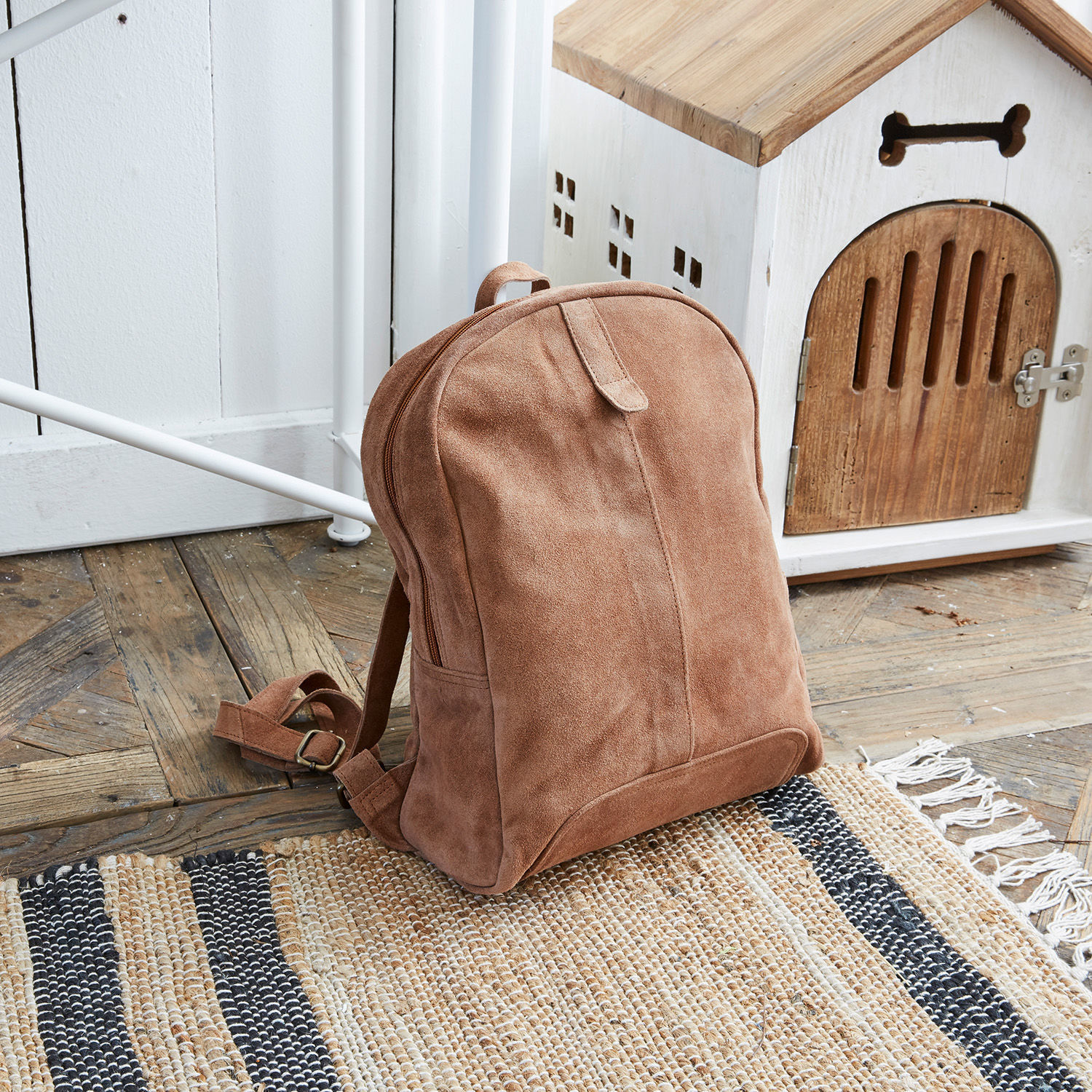 Sac à dos Palau Sac à dos en daim marron posé sur un sol en bois près d'une niche blanche en bois