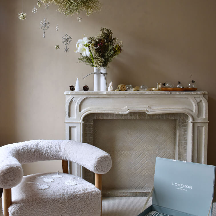 Fauteuil blanc douillet en tissu pelucheux près d'une cheminée décorative avec des flocons de neige suspendus