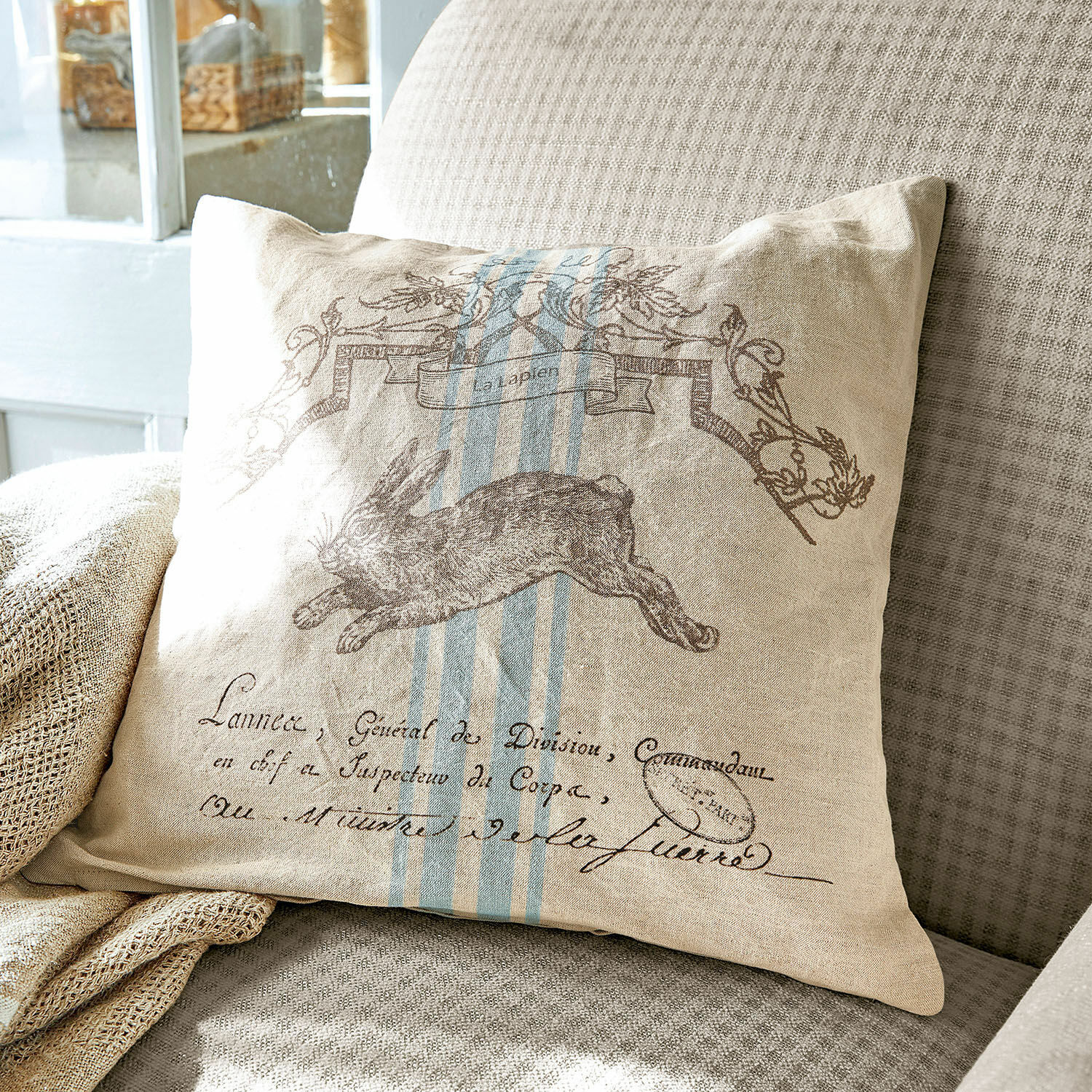 Housse de coussin La Lapin Coussin beige en lin avec imprimé de lièvre et rayures bleues sur canapé gris, décoration intérieure
