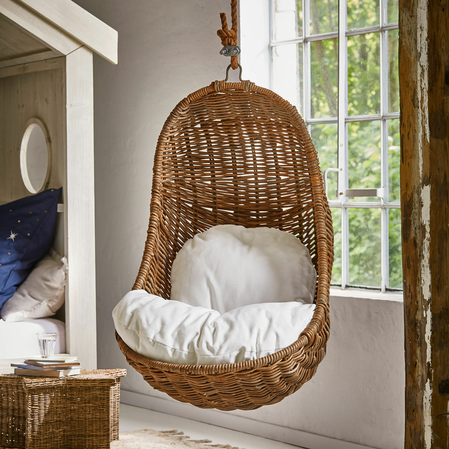 Fauteuil suspendu pour enfant Twinkla Fauteuil suspendu en rotin avec coussin blanc dans une pièce lumineuse au style naturel