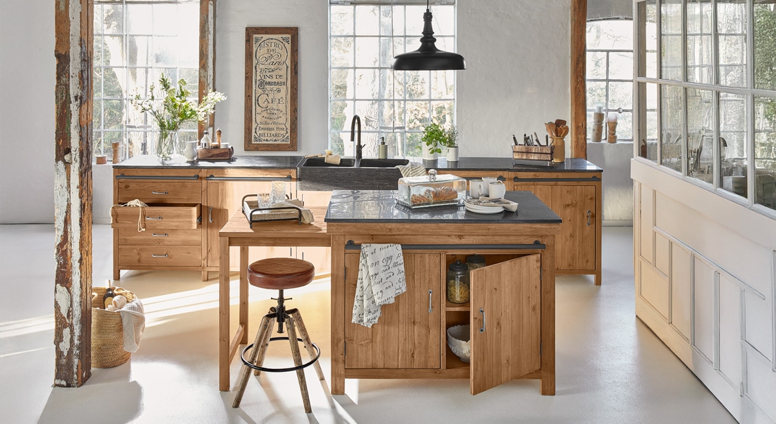Cuisine de campagne avec meubles en bois et plan de travail noir sous une lumière matinale naturelle