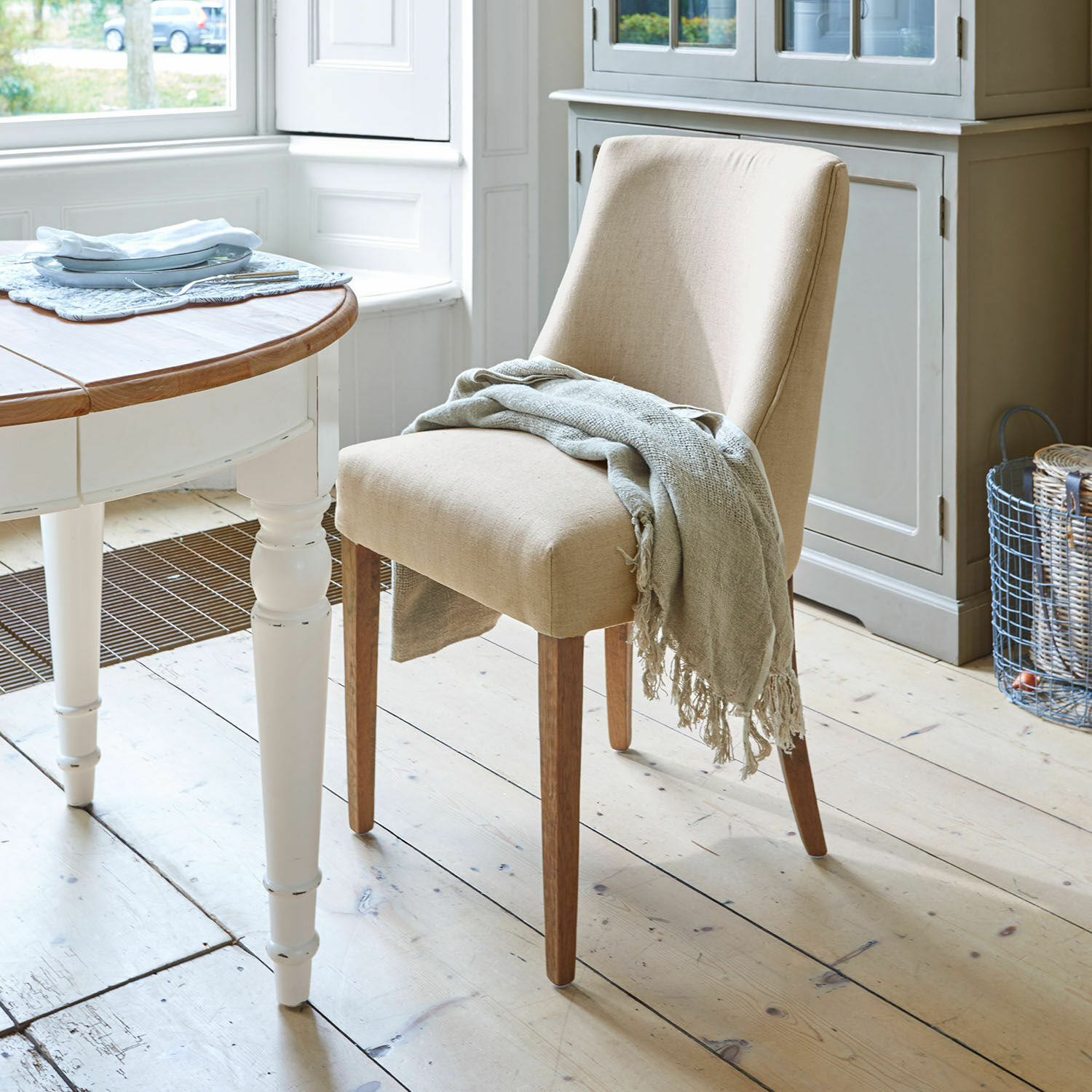 Chaise Opirel Chaise beige rembourrée avec pieds en bois et plaid gris dans une salle à manger lumineuse