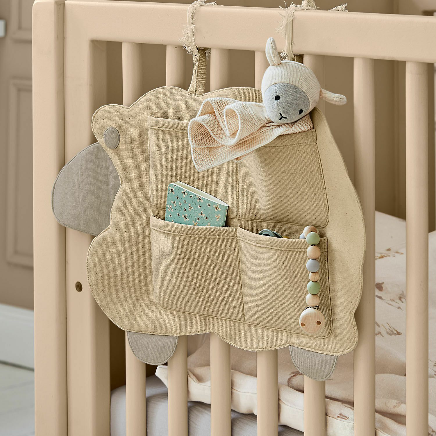 Rangement mural Erianna Organisateur beige en coton avec poches et peluche mouton accroché à un lit bébé en bois