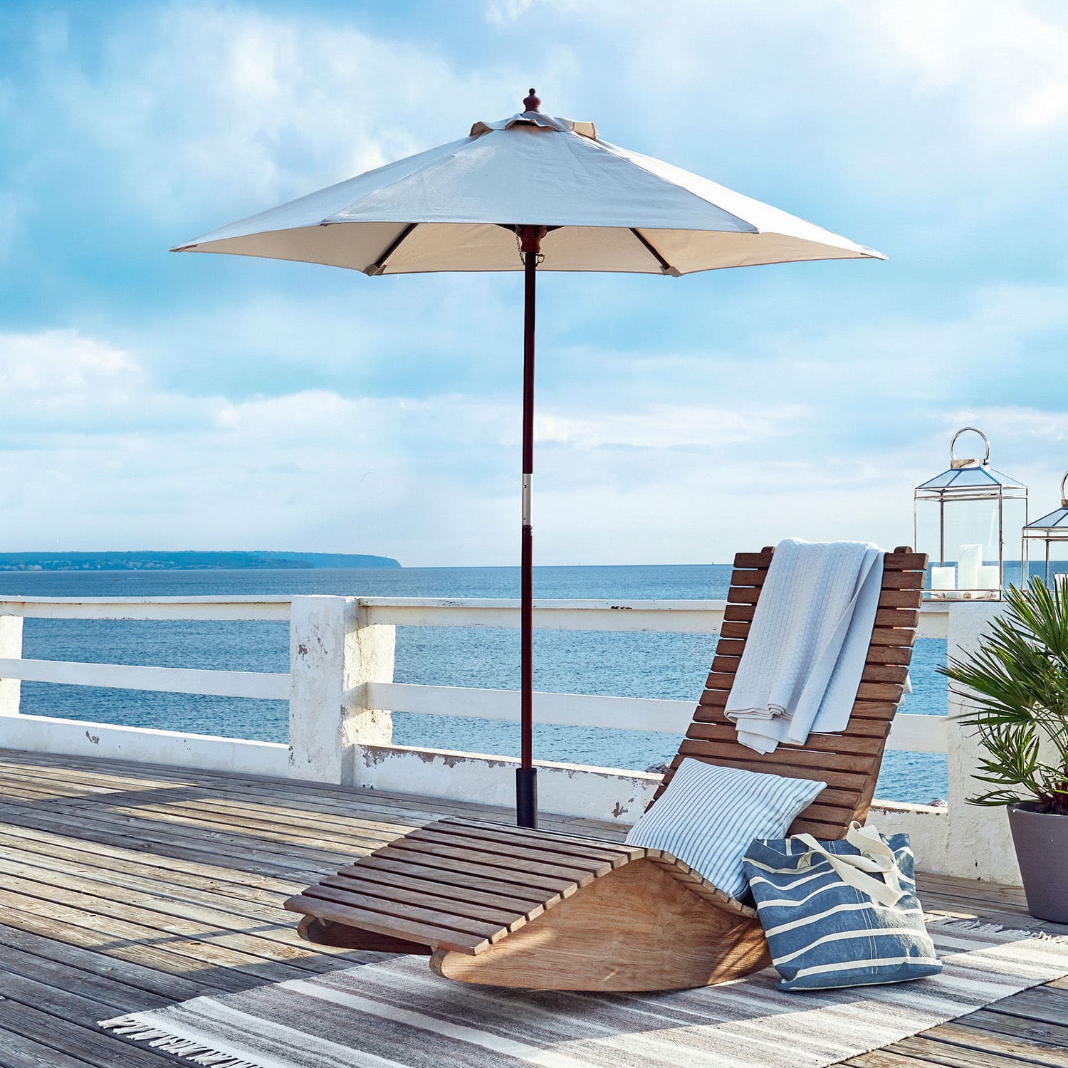 Chaise longue en bois de teck naturel avec parasol et coussin sur terrasse face à la mer