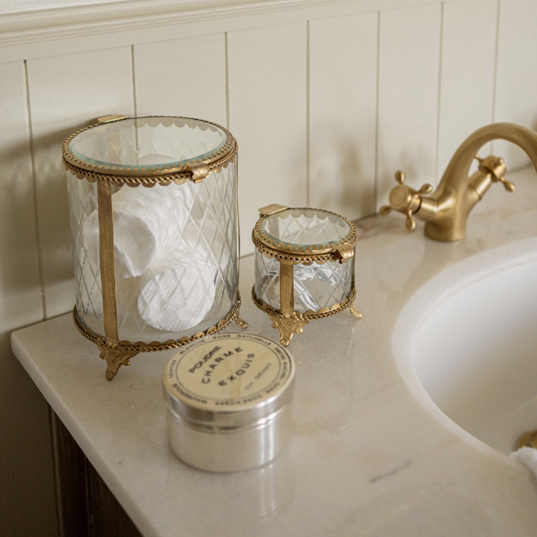 Boîtes en verre avec ornements en laiton pour cotons et cosmétiques sur plan de salle de bain en marbre