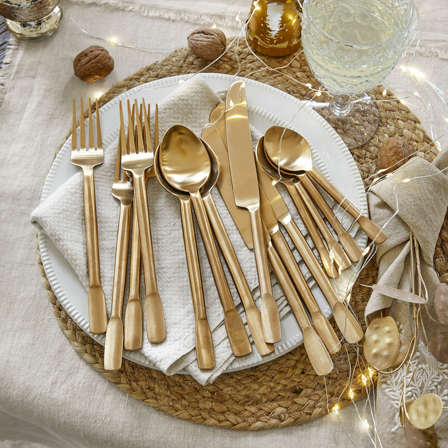 Couverts Malroy Ensemble de couverts dorés en acier inoxydable sur une assiette blanche avec décoration festive et guirlandes LED