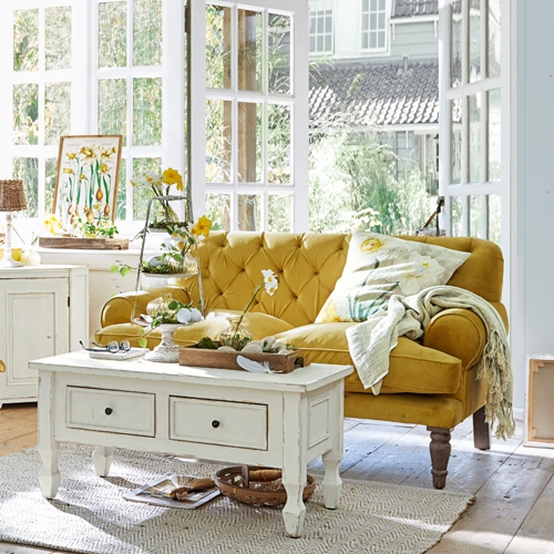 Canapé jaune en velours style vintage dans un salon lumineux avec table basse blanche en bois et décorations