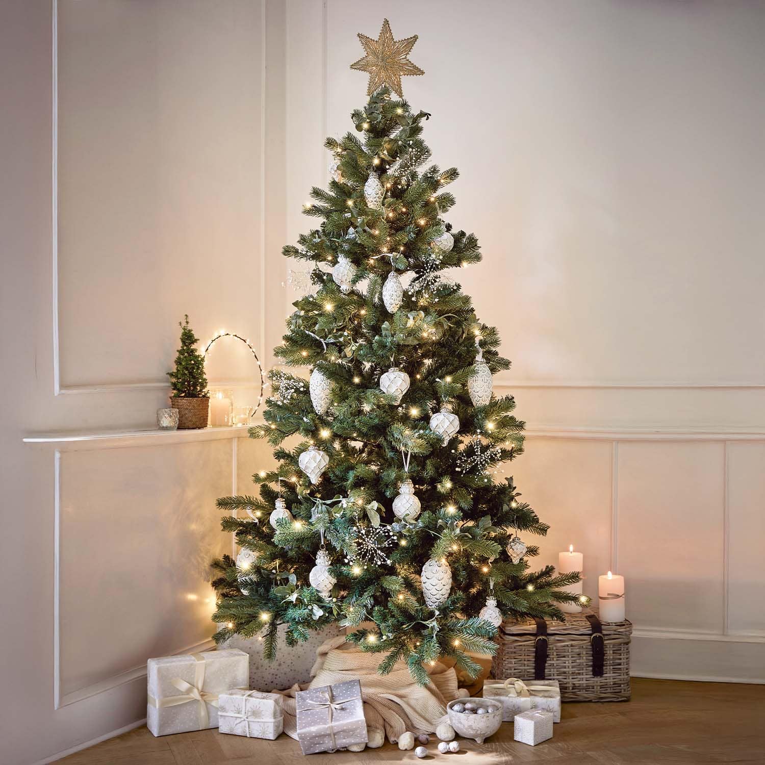 Sapin de Noël décoré avec boules blanches et guirlandes lumineuses, cadeaux et bougies dans un intérieur chaleureux