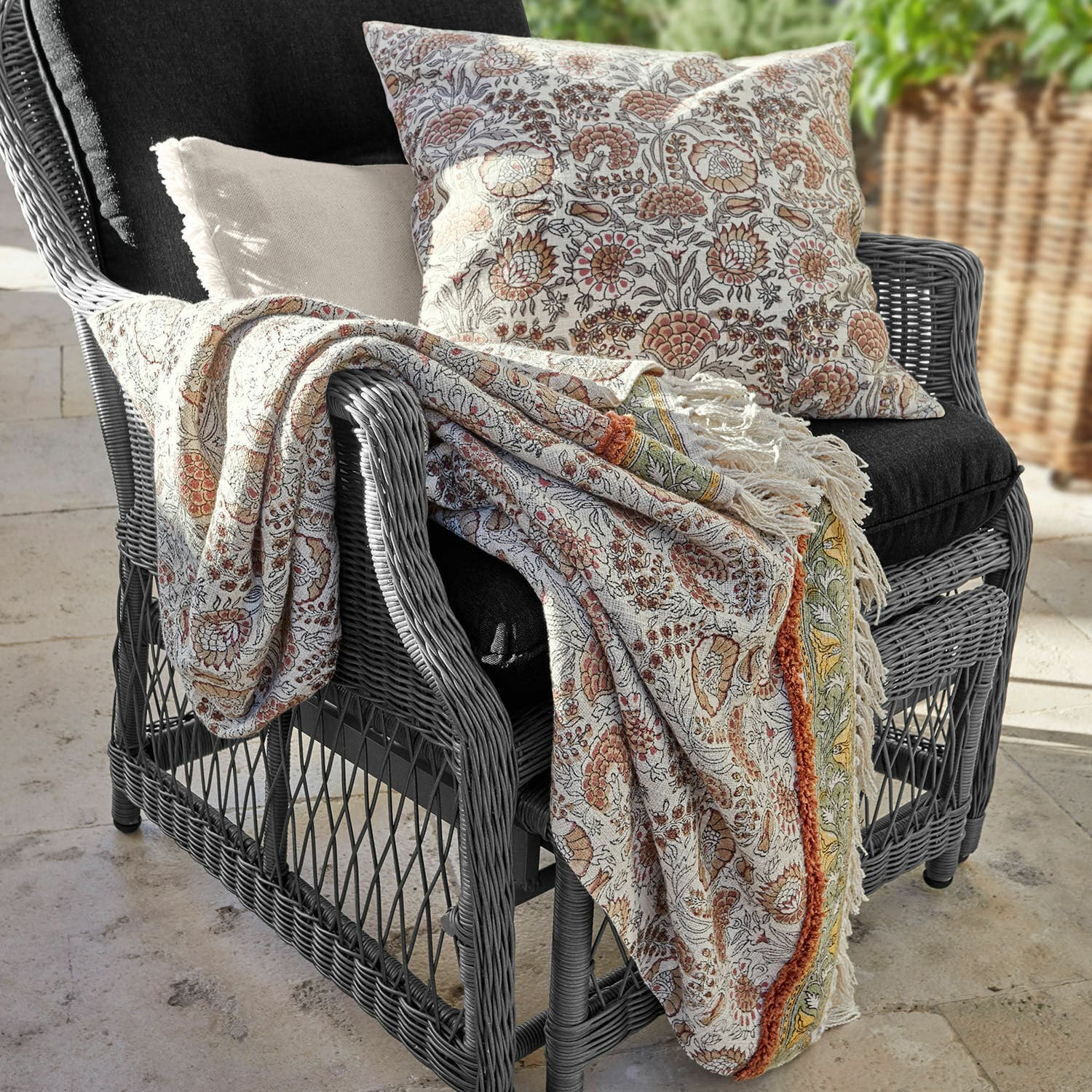 Plaid Romila Plaid et coussin en coton à motif floral chaud sur fauteuil gris en rotin pour décoration intérieure